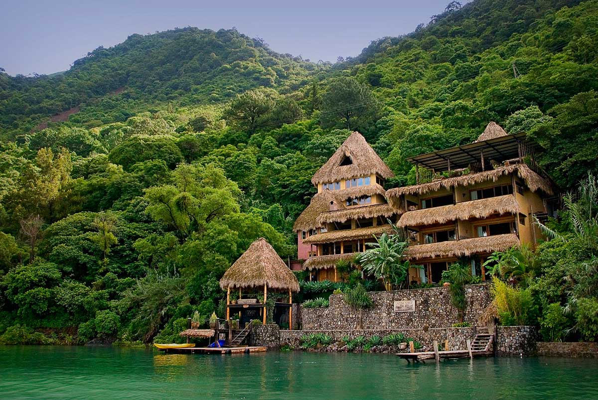 Lakeside exterior with thatched roofs against a forested hillside, Laguna Lodge, Lake Atitlán, Guatemala
