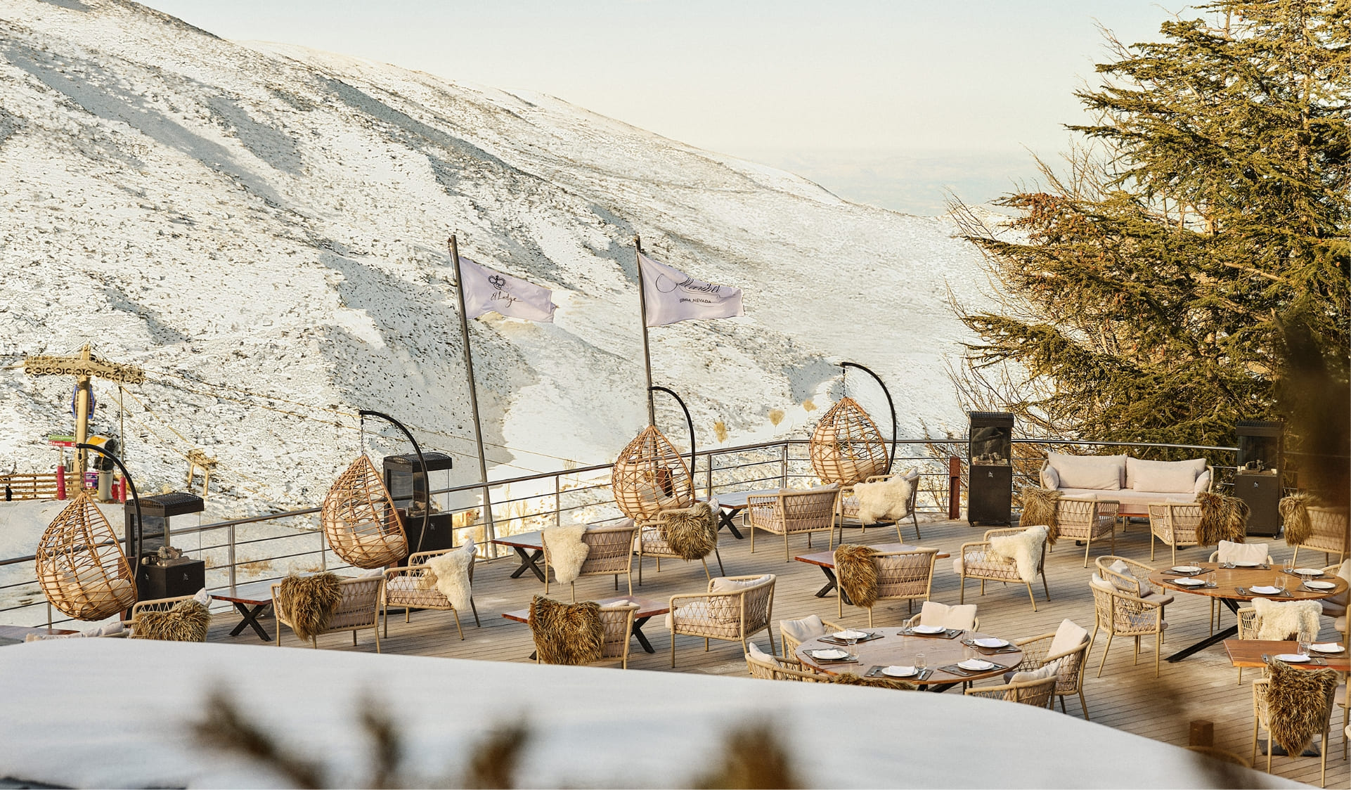 Dining terrace with hanging chairs facing a snowy mountain slope at El Lodge, Sierra Nevada, Spain