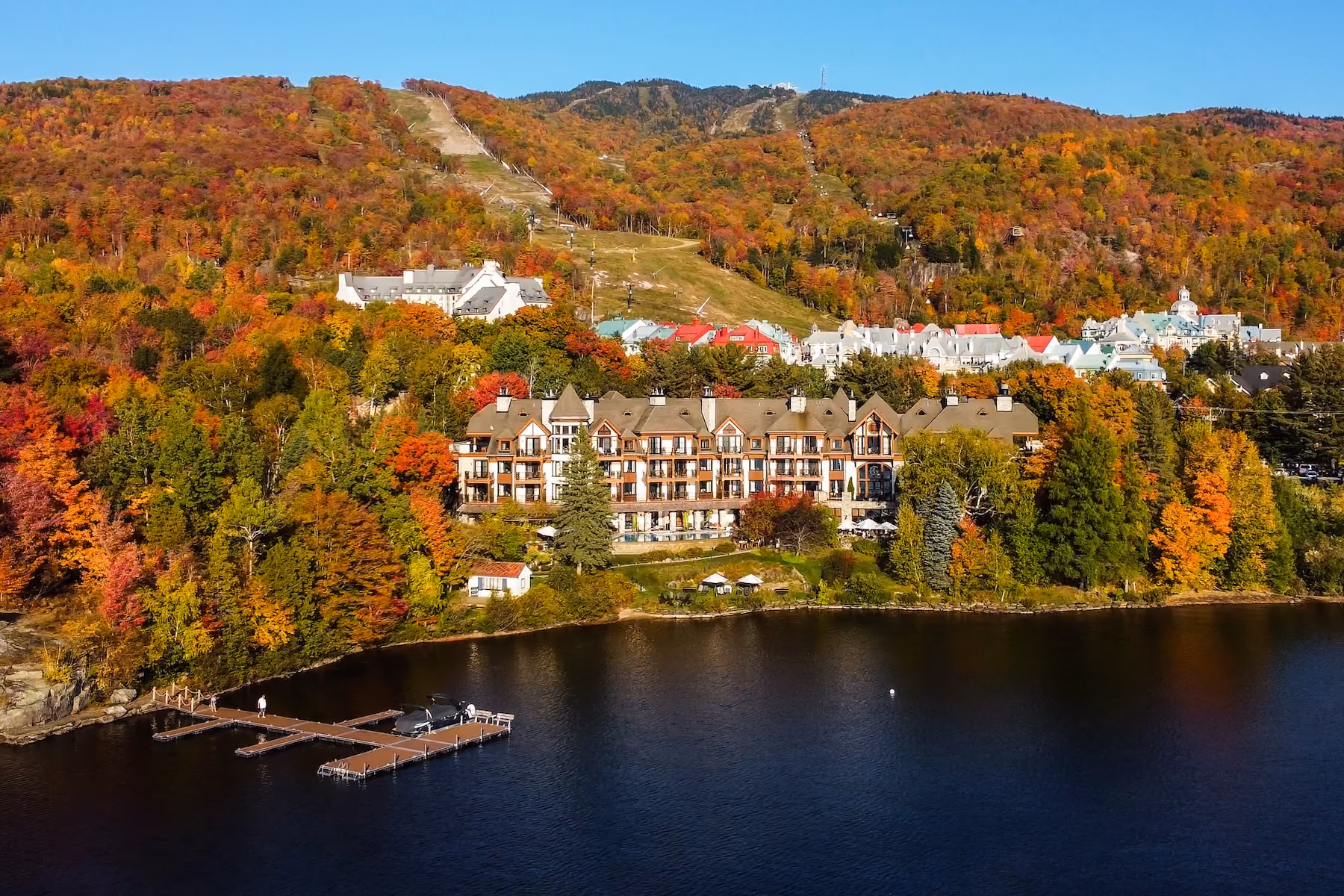 Lakeside hotel exterior surrounded by autumn foliage, with balconies facing Lake Tremblant and a dock along the shore at Hôtel Quintessence