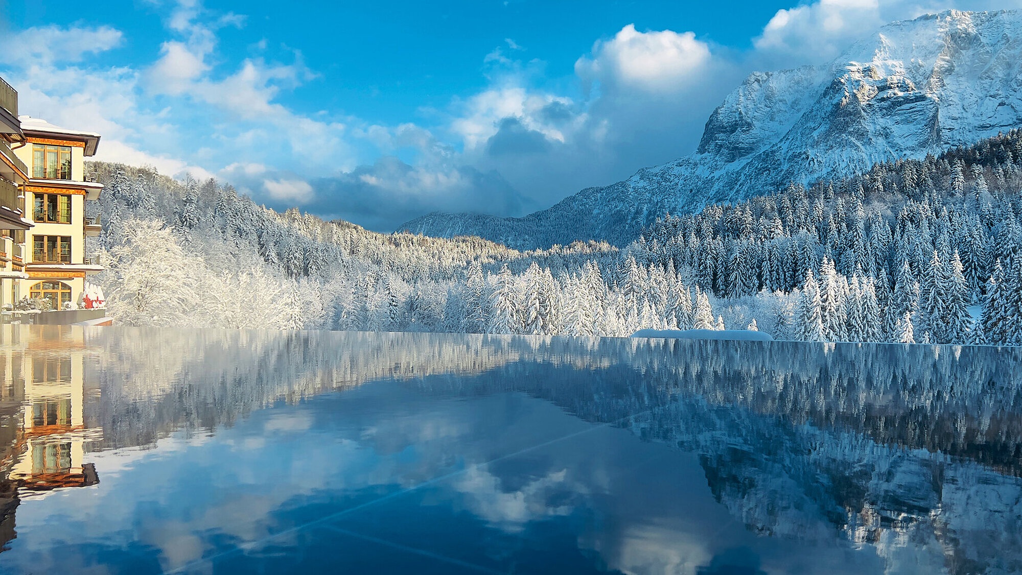 Lake reflecting snowy mountains beside hotel at Schloss Elmau, Bavarian Alps, Germany
