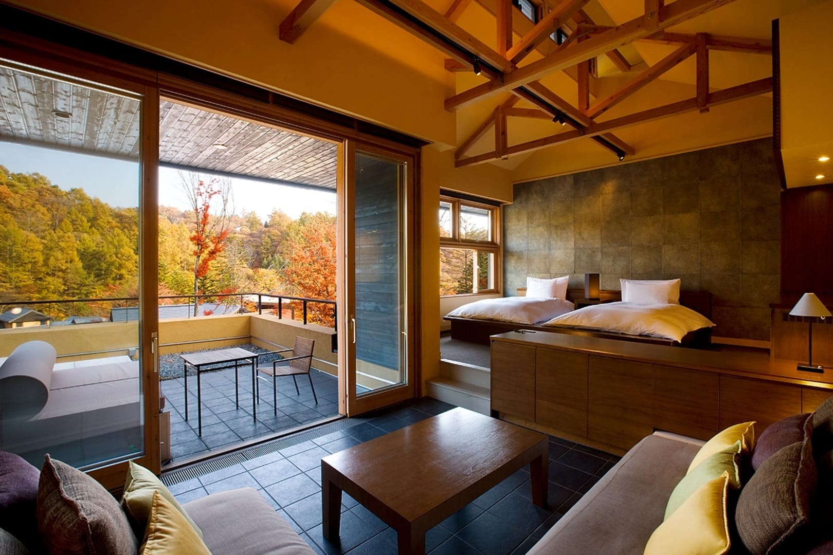 Guest room with exposed wooden ceiling beams, a low bed and a terrace opening toward autumn trees, Hoshinoya Karuizawa