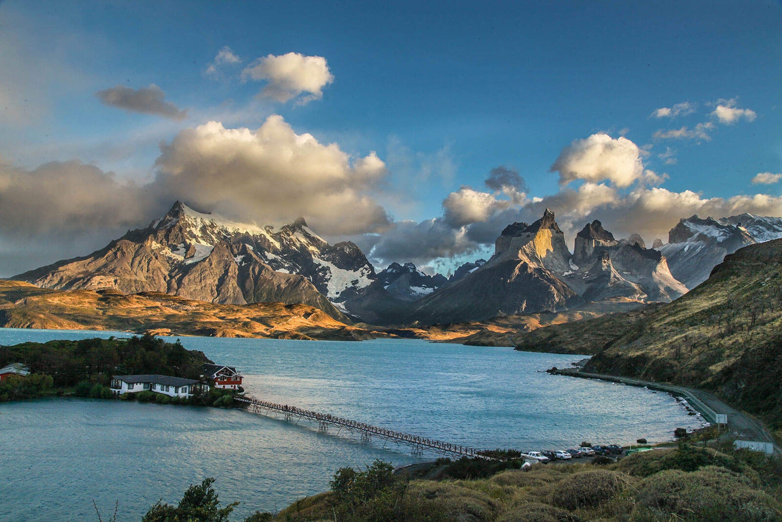 Wide lake view of the island lodge, footbridge and rugged mountain skyline at Hostería Pehoé, Torres del Paine, Chile