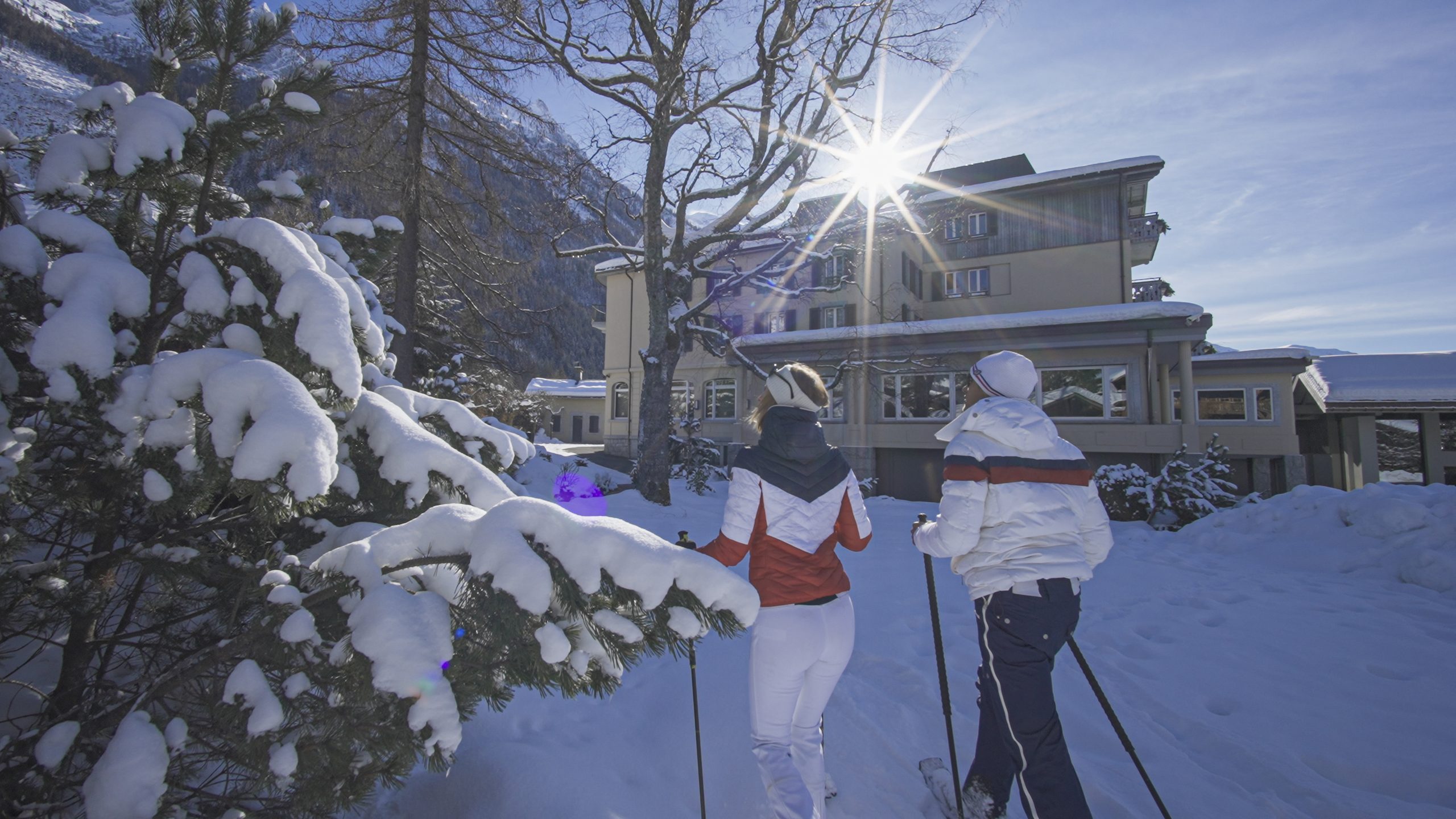 Snowshoe walkers approaching the hotel through a sunlit snowy garden, Le Hameau Albert 1er, Chamonix, France