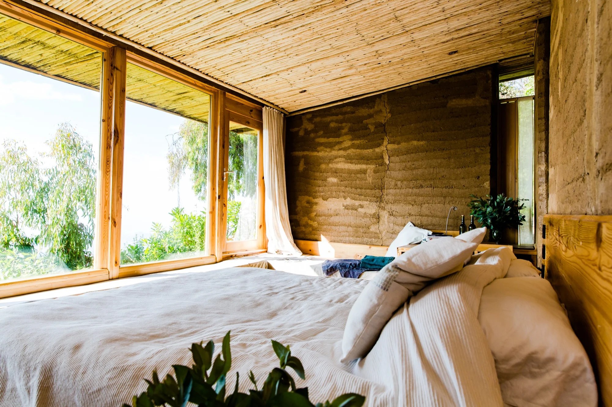Bed beside broad picture windows looking onto trees at Limalimo Lodge.