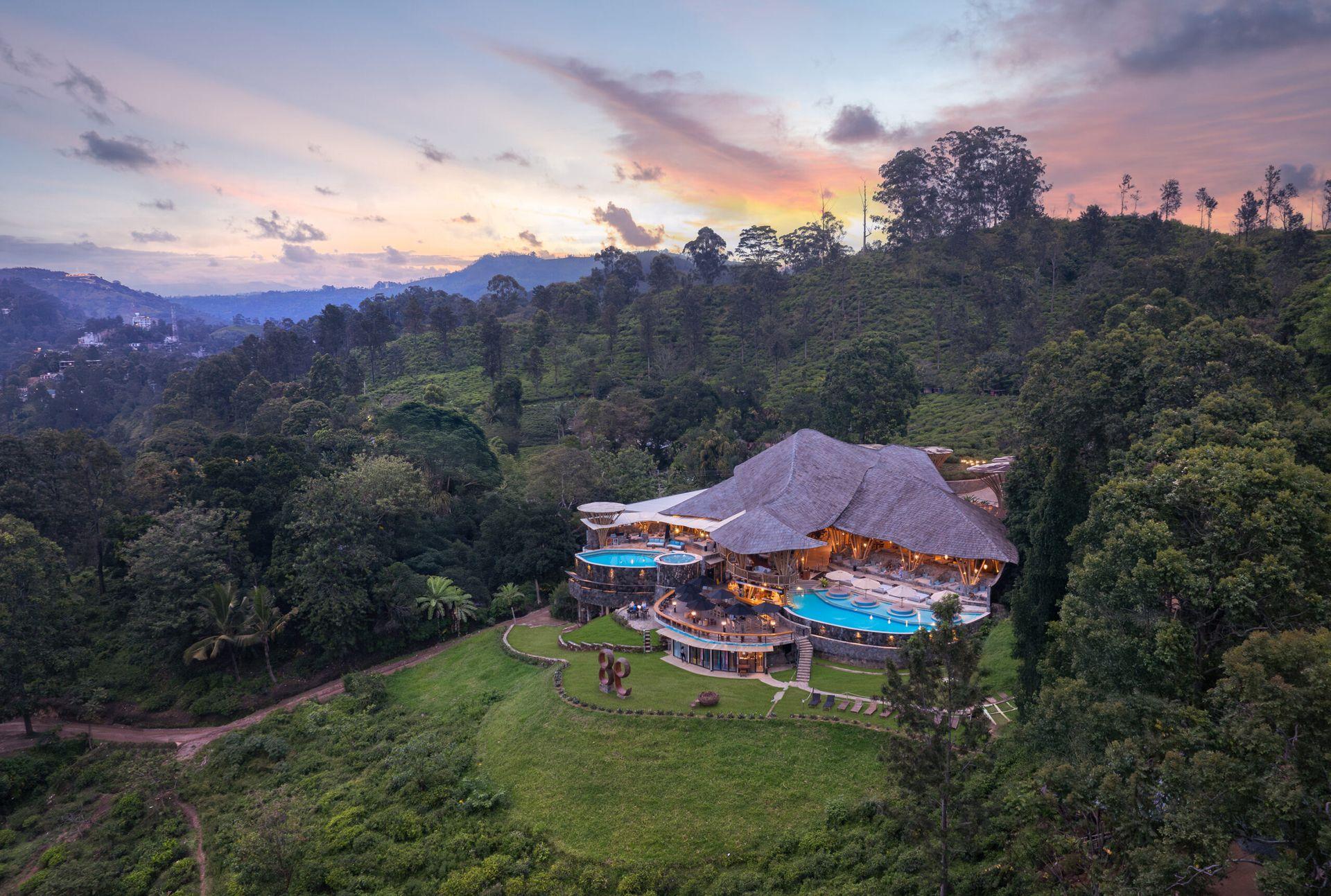 Ravana Pool Club illuminated at sunset amid wooded hills, 98 Acres Resort, Ella, Sri Lanka