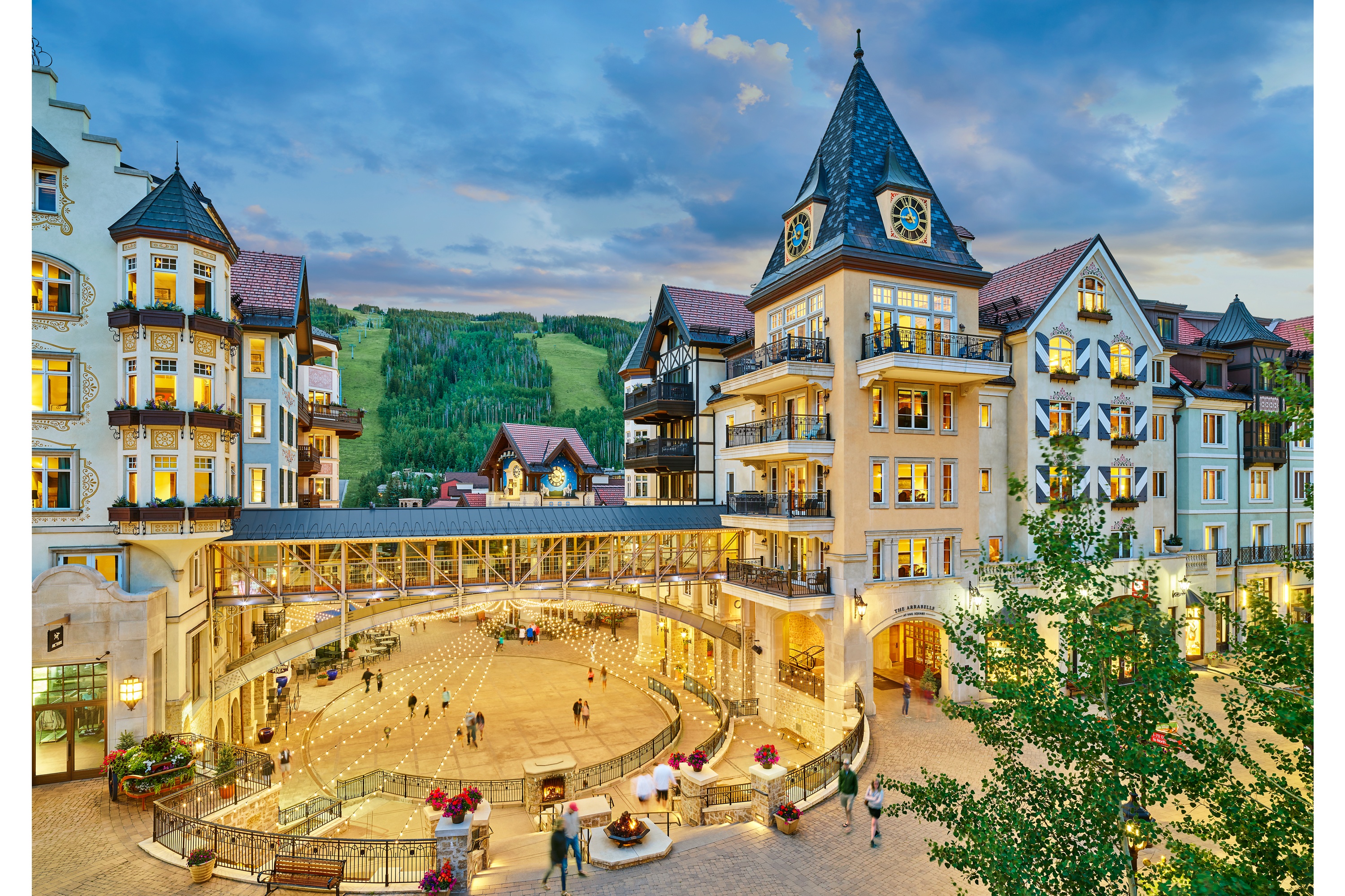 The Arrabelle at Vail Square illuminated above its outdoor winter ice rink, with skaters and Vail Mountain beyond.