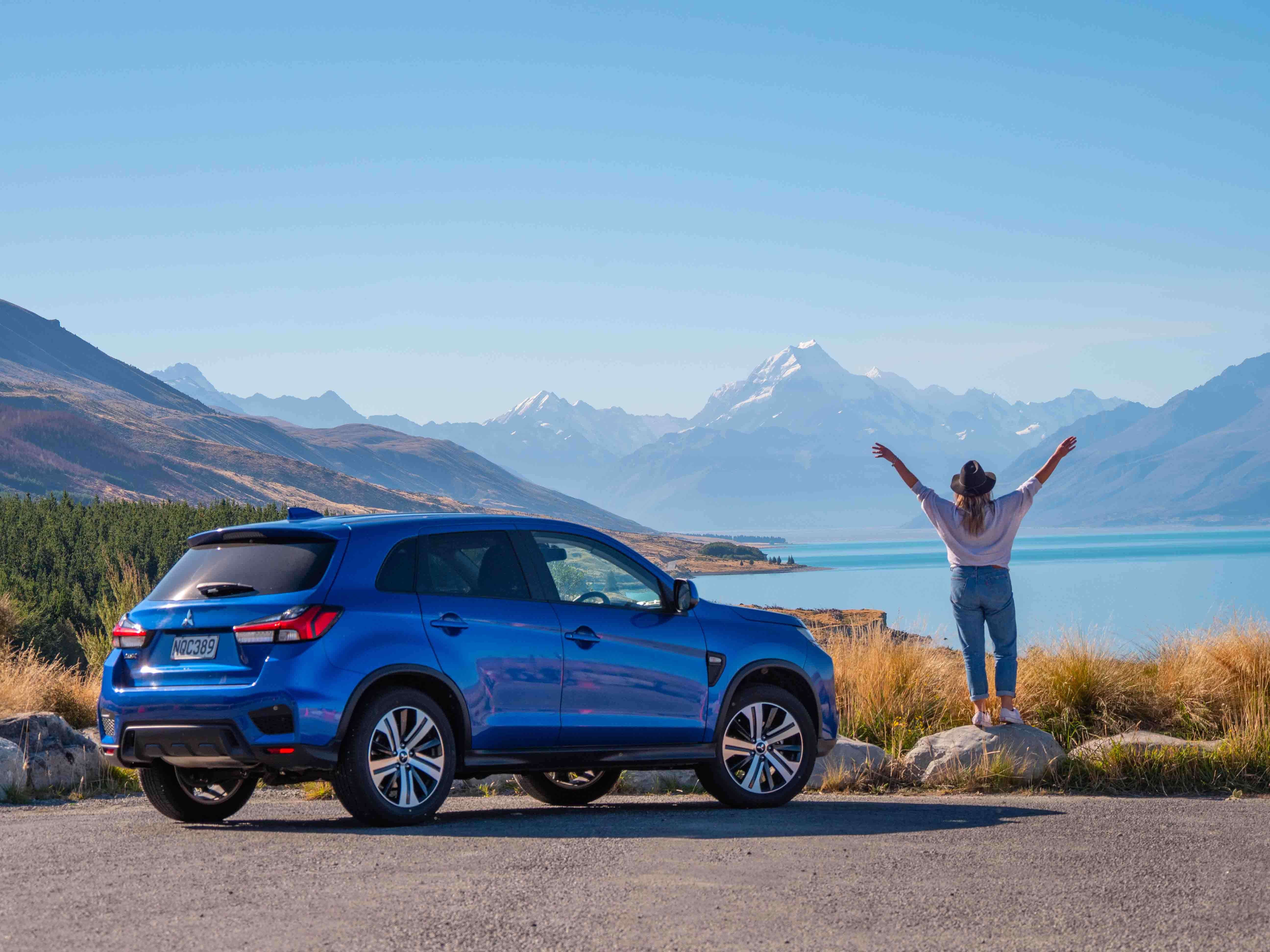 Blue car and traveller at a lakeside viewpoint with distant Aoraki/Mount Cook at The Hermitage Hotel, Aoraki/Mount Cook