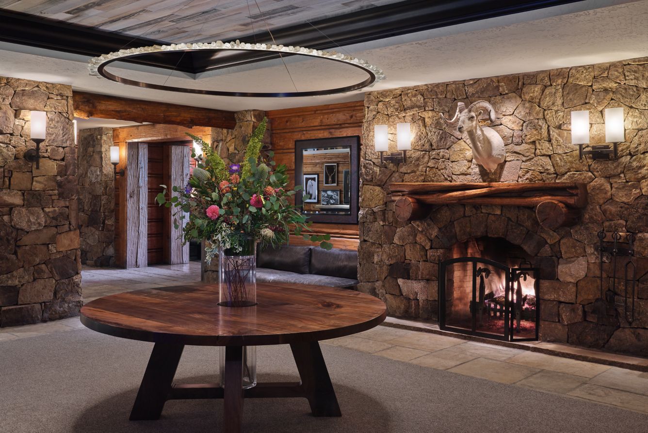 Stone fireplace, flowers and round wooden table in the entrance lobby at The Ritz-Carlton, Bachelor Gulch.