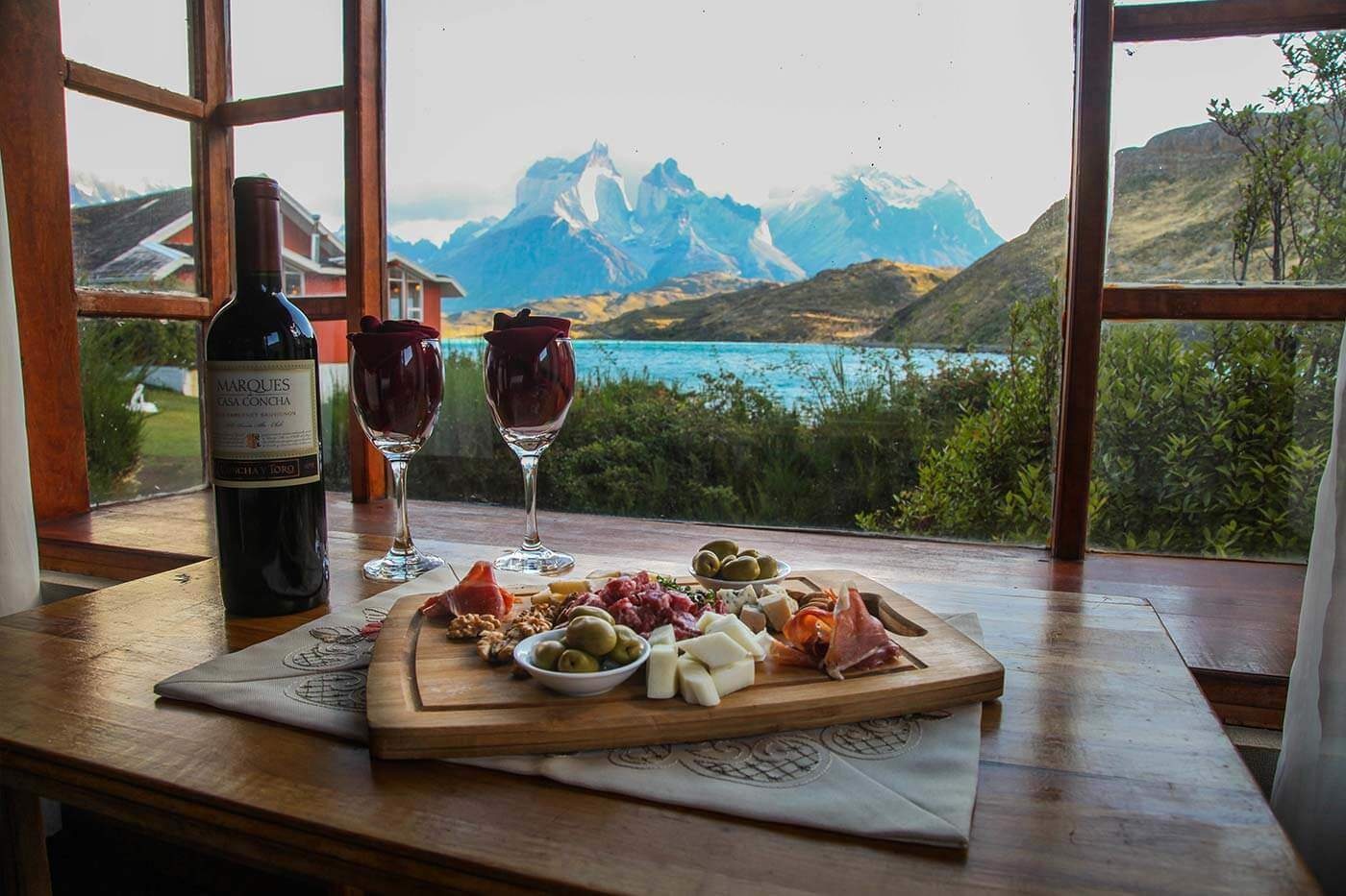 Wine glasses and a food board beside a window overlooking the lake and peaks at Hostería Pehoé, Torres del Paine, Chile