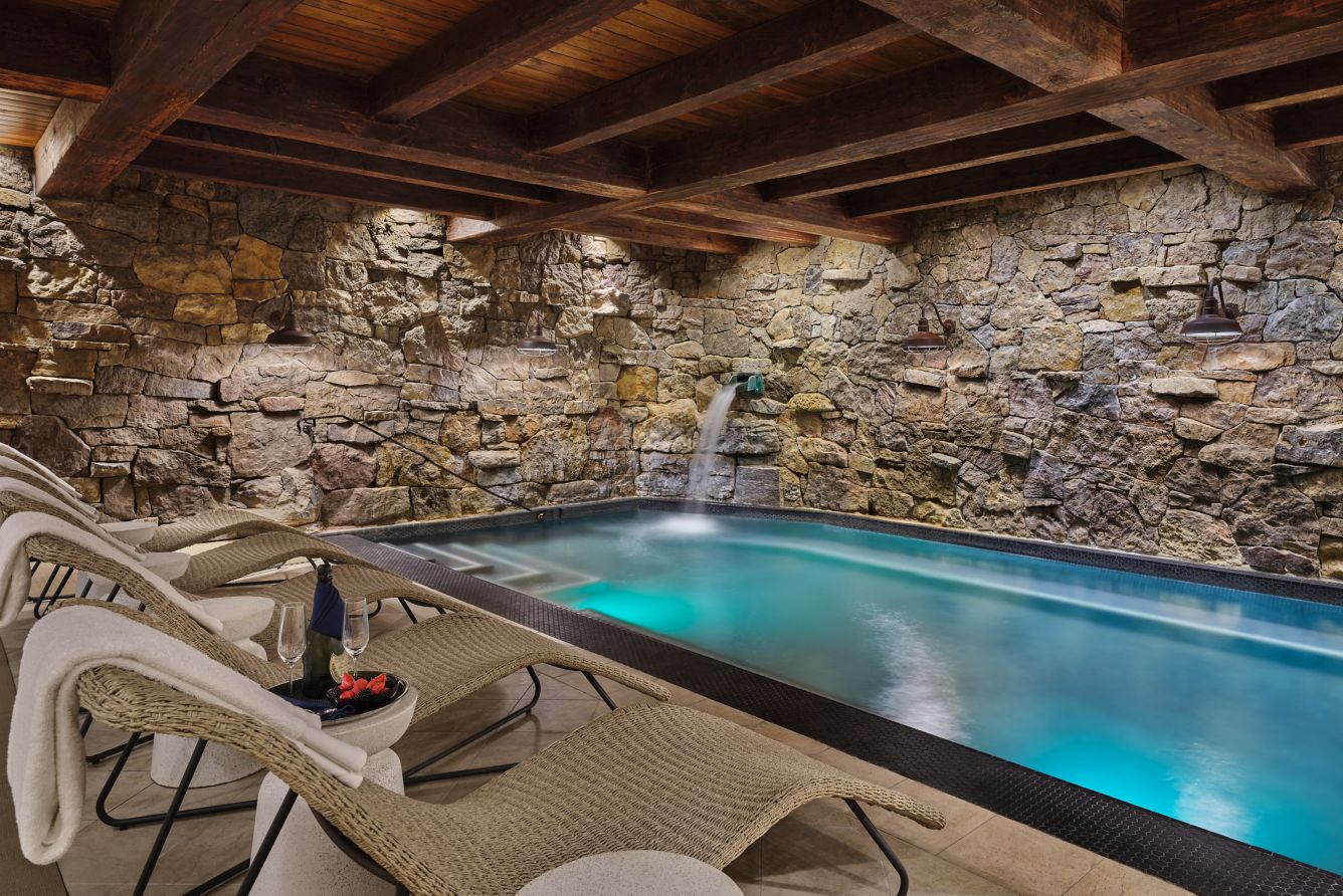 Rock-walled Grotto spa pool with loungers beneath timber beams at The Ritz-Carlton, Bachelor Gulch.