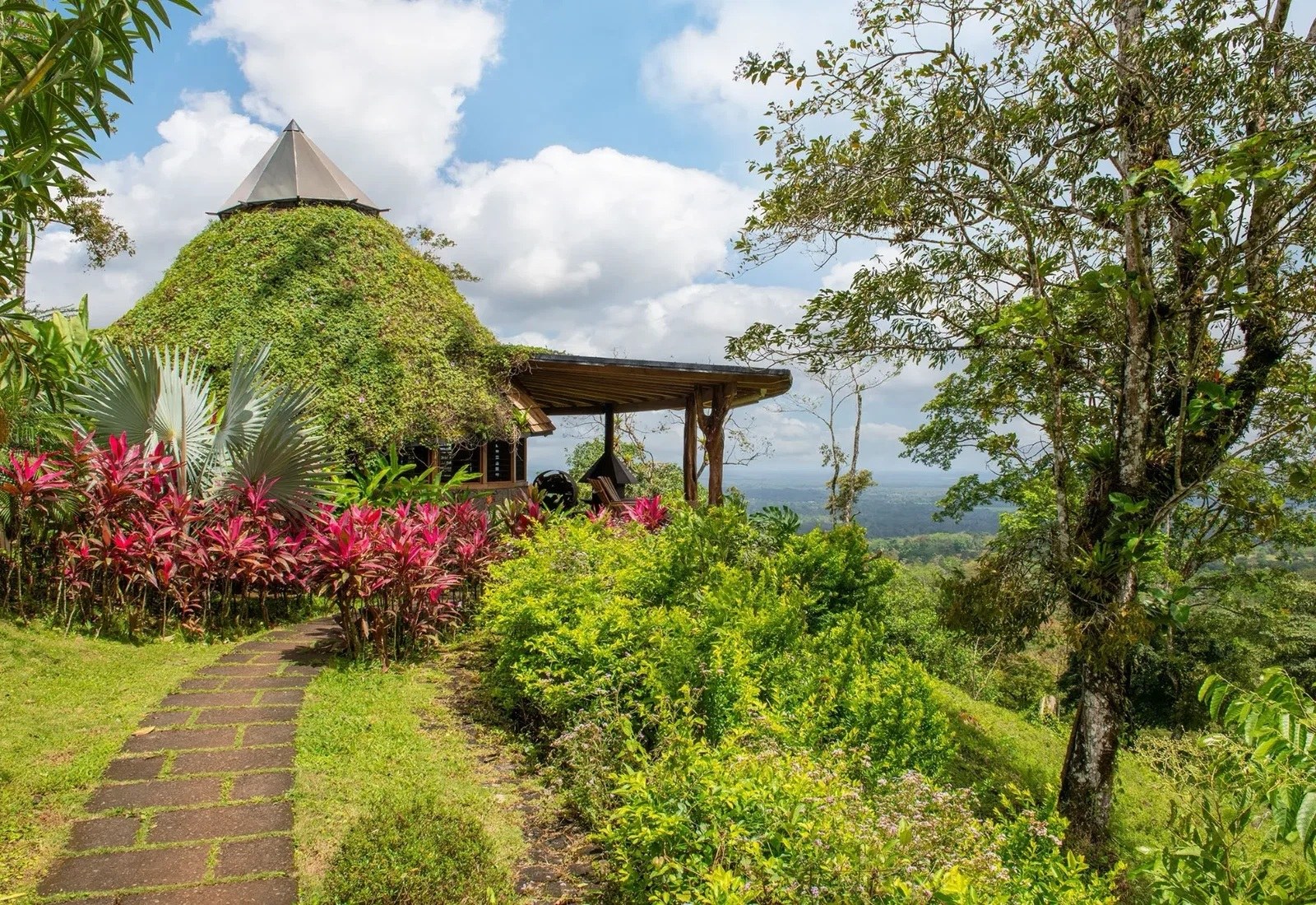 Green-roofed circular lodge beside a garden path on the wooded hillside at Origins Floral, Origins Luxury Lodge
