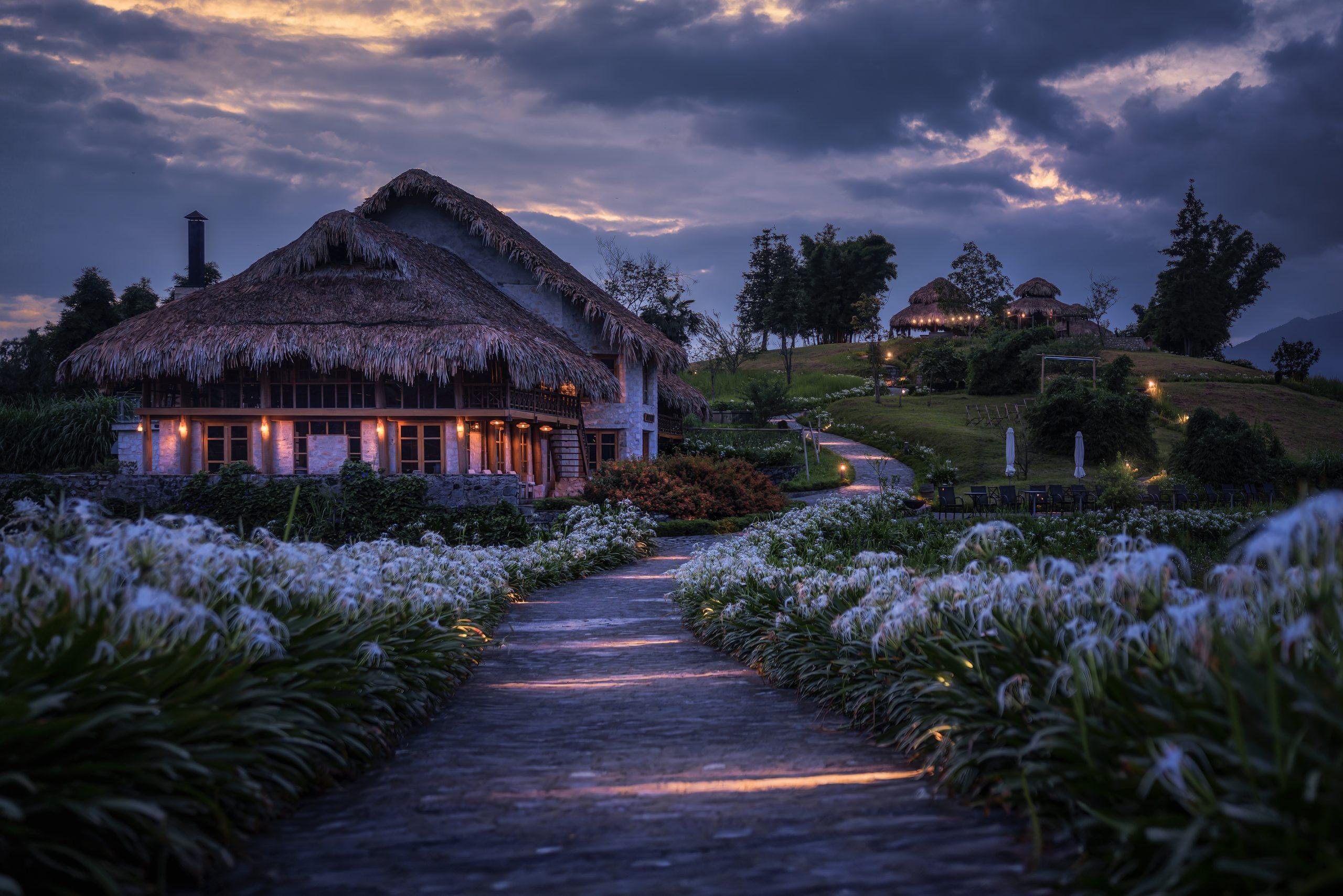Thatched pavilion exterior and garden path illuminated at twilight, Topas Ecolodge, Sapa, Vietnam