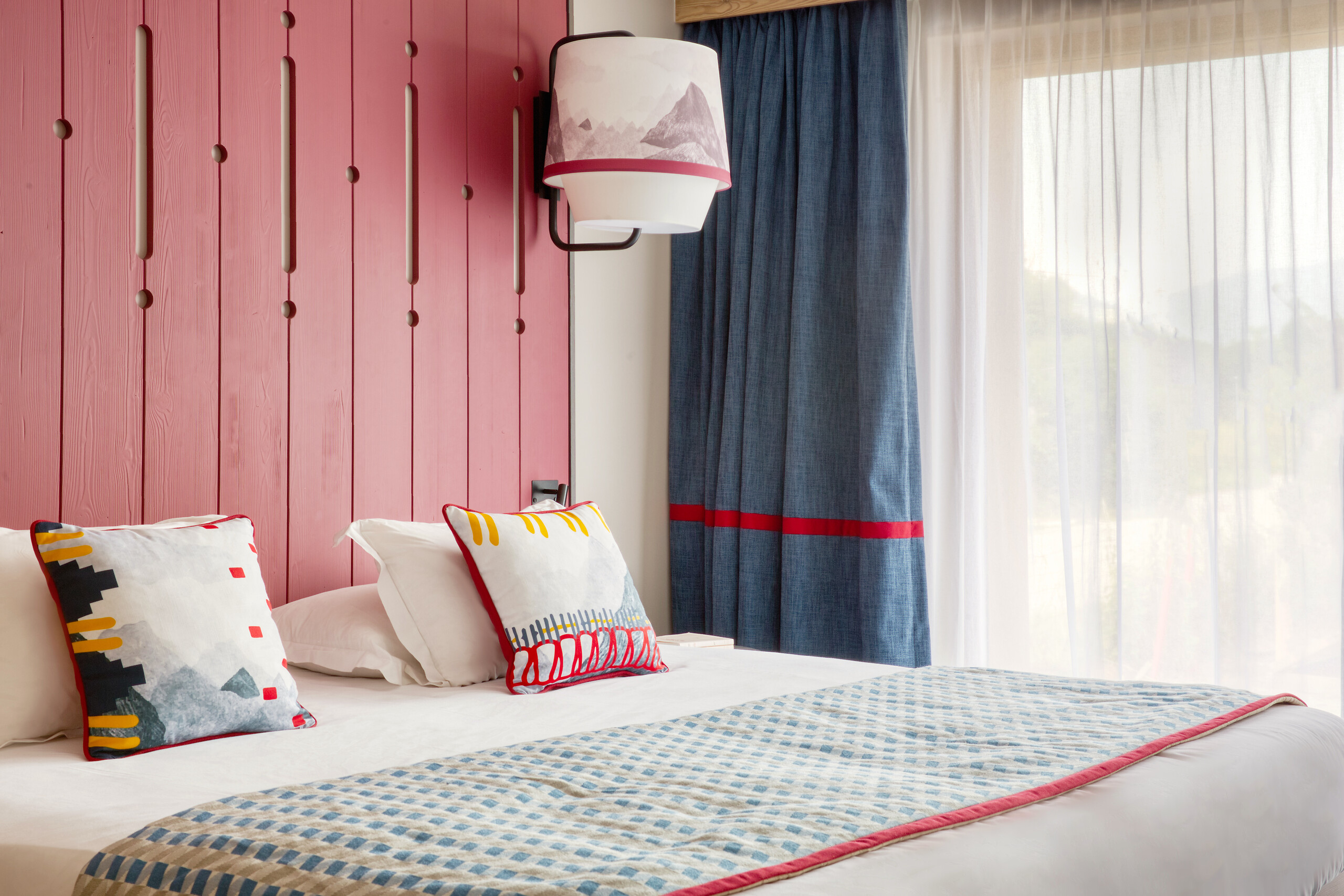 Superior room with a pink timber headboard, colourful cushions and a window at Club Med Tignes