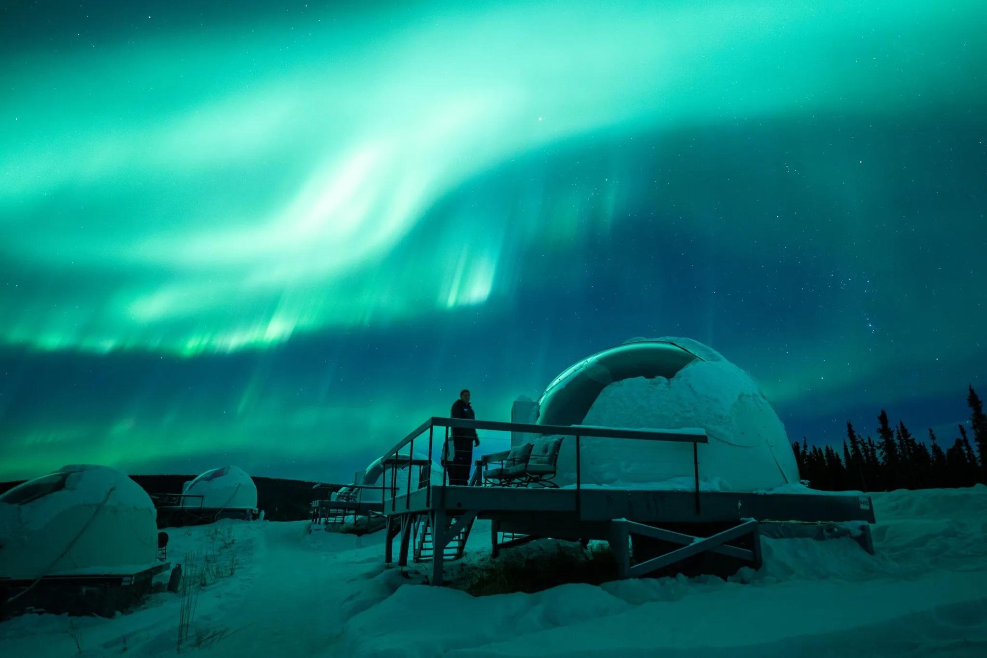 Aurora ribbons above snow-covered igloos, Borealis Basecamp, Alaska, USA