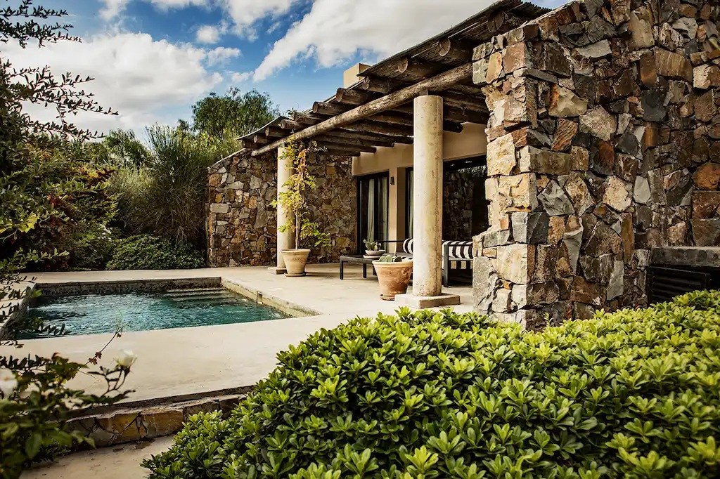 Private plunge pool and shaded terrace beside a rustic stone villa surrounded by greenery, Cavas Wine Lodge