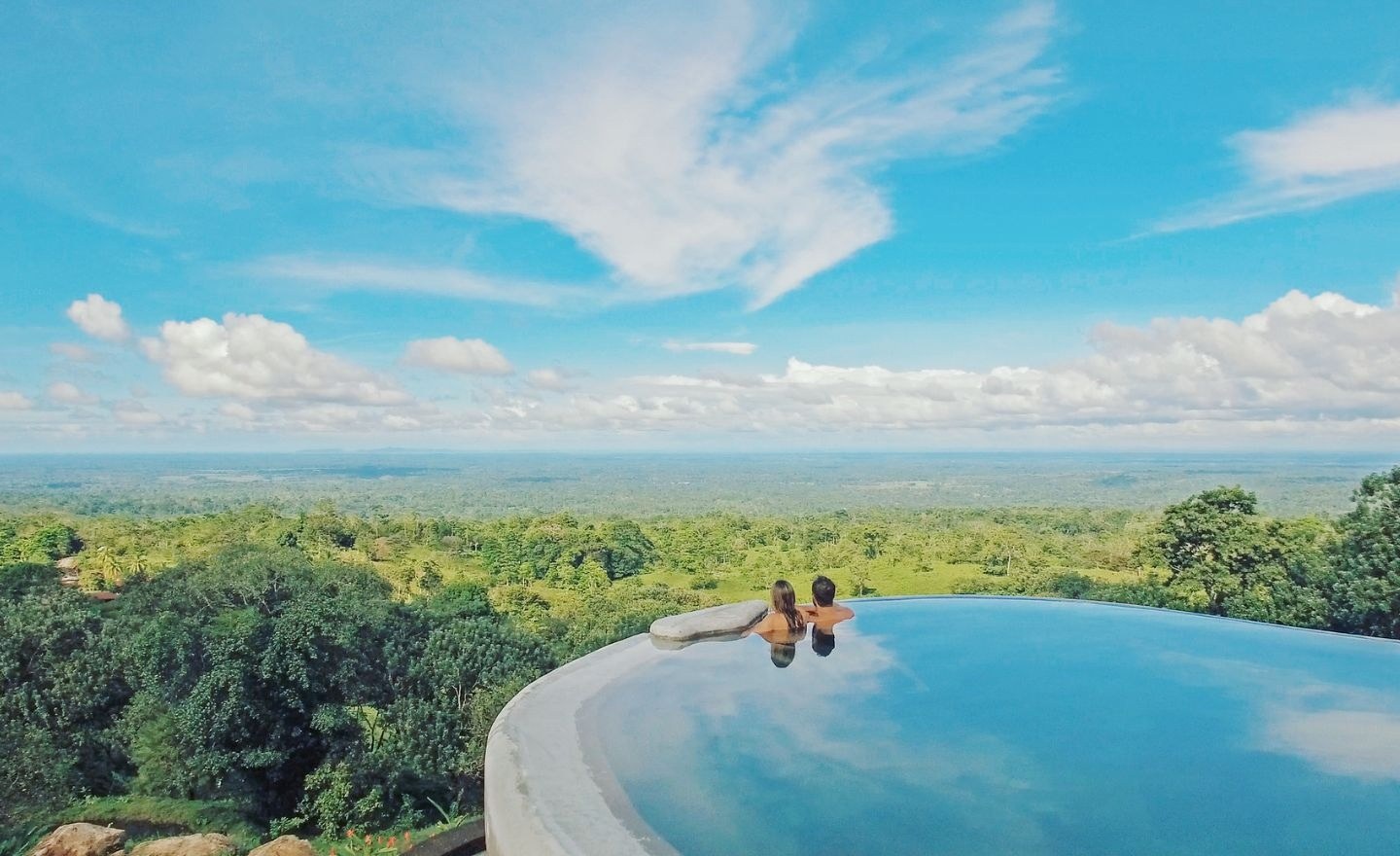 Guests in the infinity pool overlooking forest and the distant valley, Origins Luxury Lodge