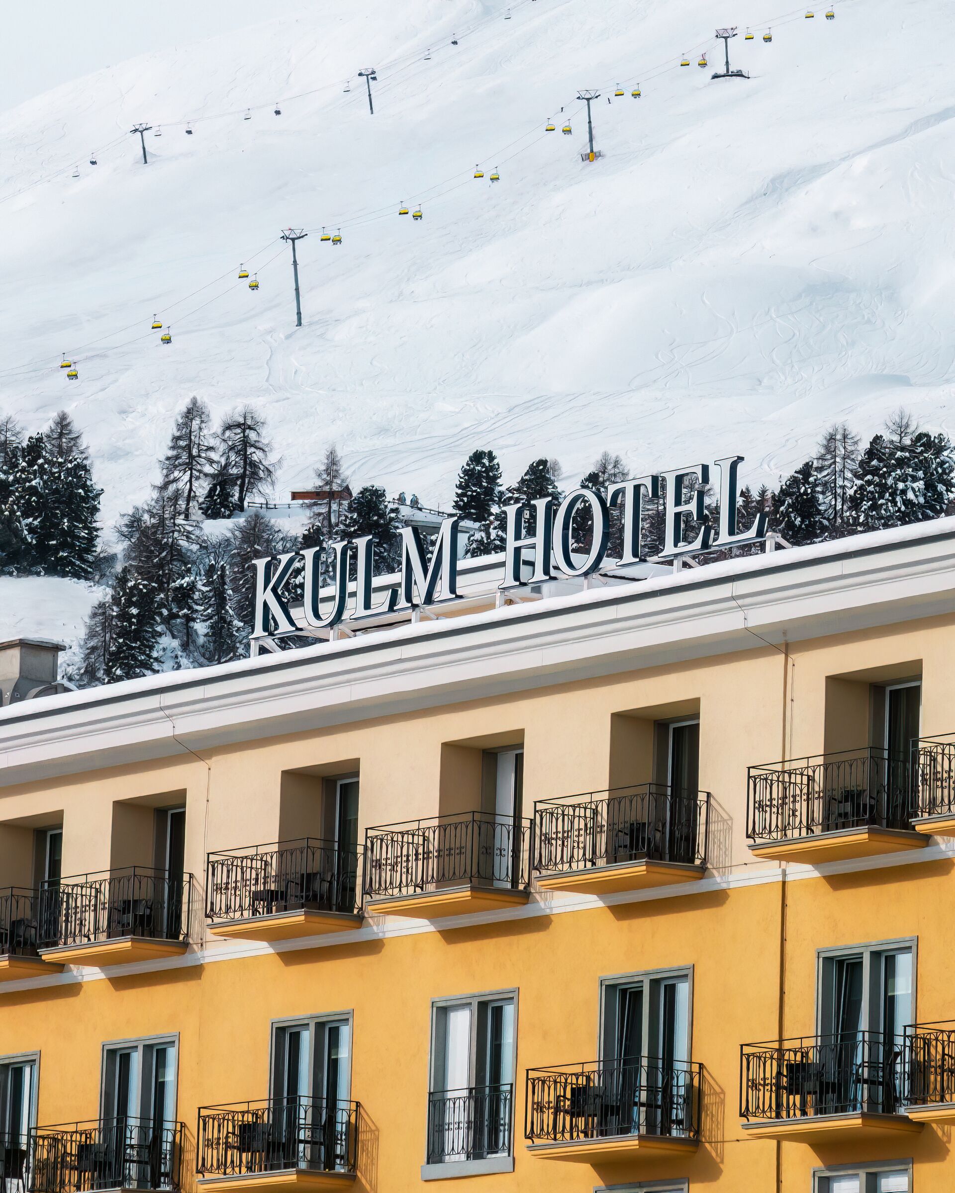 Yellow hotel facade below the snow-covered slopes, Kulm Hotel St. Moritz, St. Moritz, Switzerland
