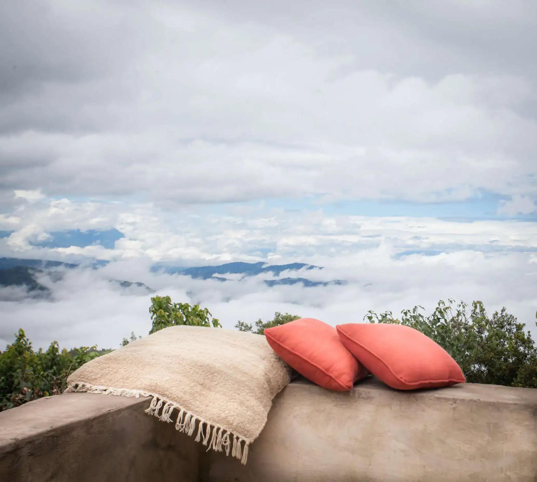 Cushioned outdoor seat with a view over clouds and distant hills, Clouds Mountain Gorilla Lodge, Bwindi Impenetrable National Park, Uganda