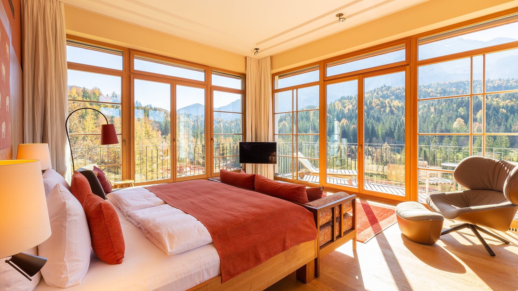 Bedroom with red bedding and large windows over forest at Schloss Elmau, Bavarian Alps, Germany