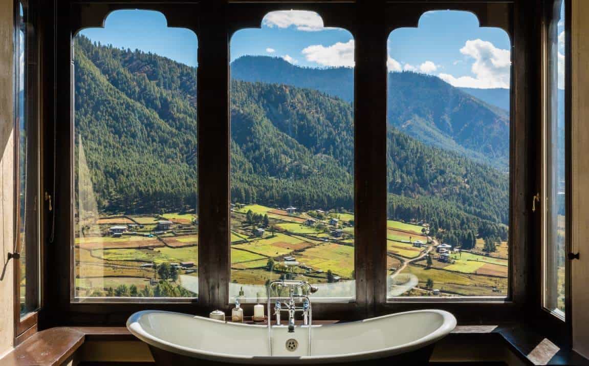 Freestanding bathtub beside timber-framed suite windows overlooking fields in the Phobjikha Valley at Gangtey Lodge