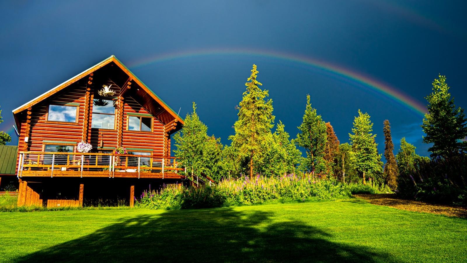 Log lodge beside Judd Lake beneath a rainbow, Tordrillo Mountain Lodge, Alaska, USA