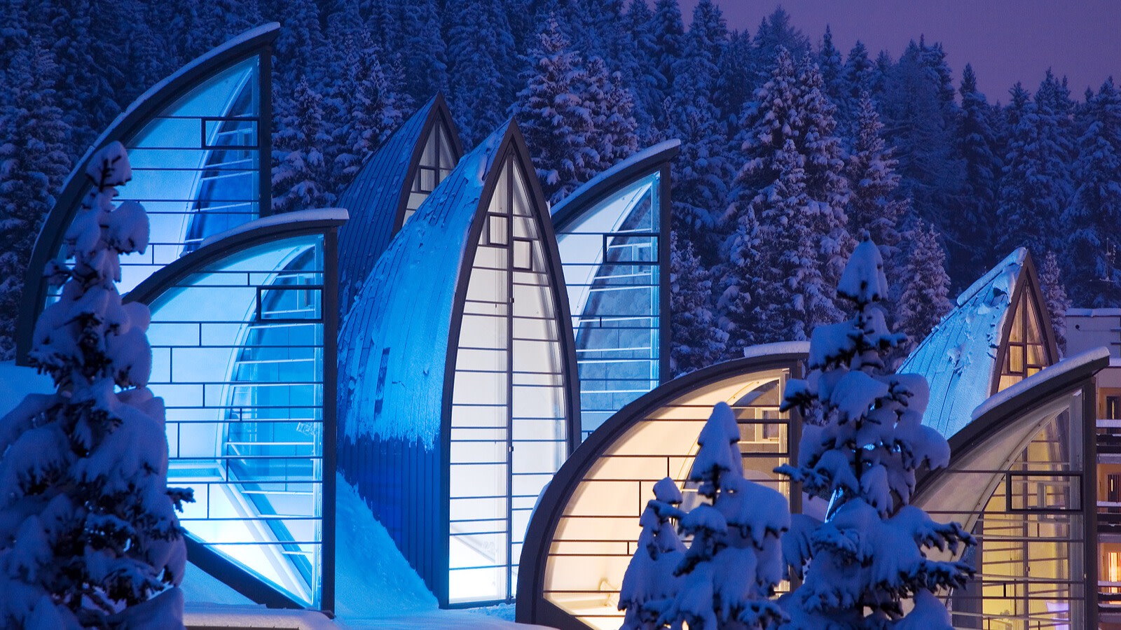 Tschuggen Bergoase's illuminated glass sails among snowy forest trees, Arosa, Switzerland