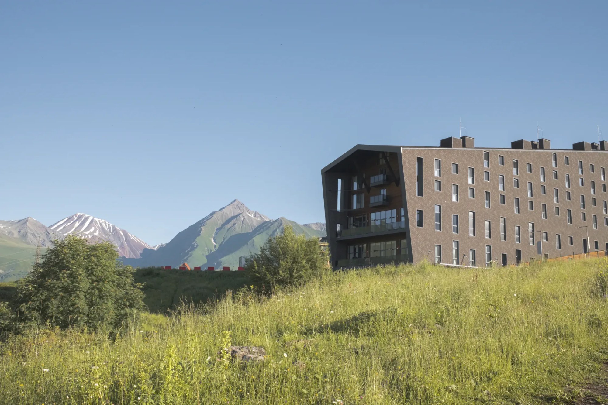 Gudauri Lodge exterior on a grassy slope below the Caucasus mountains