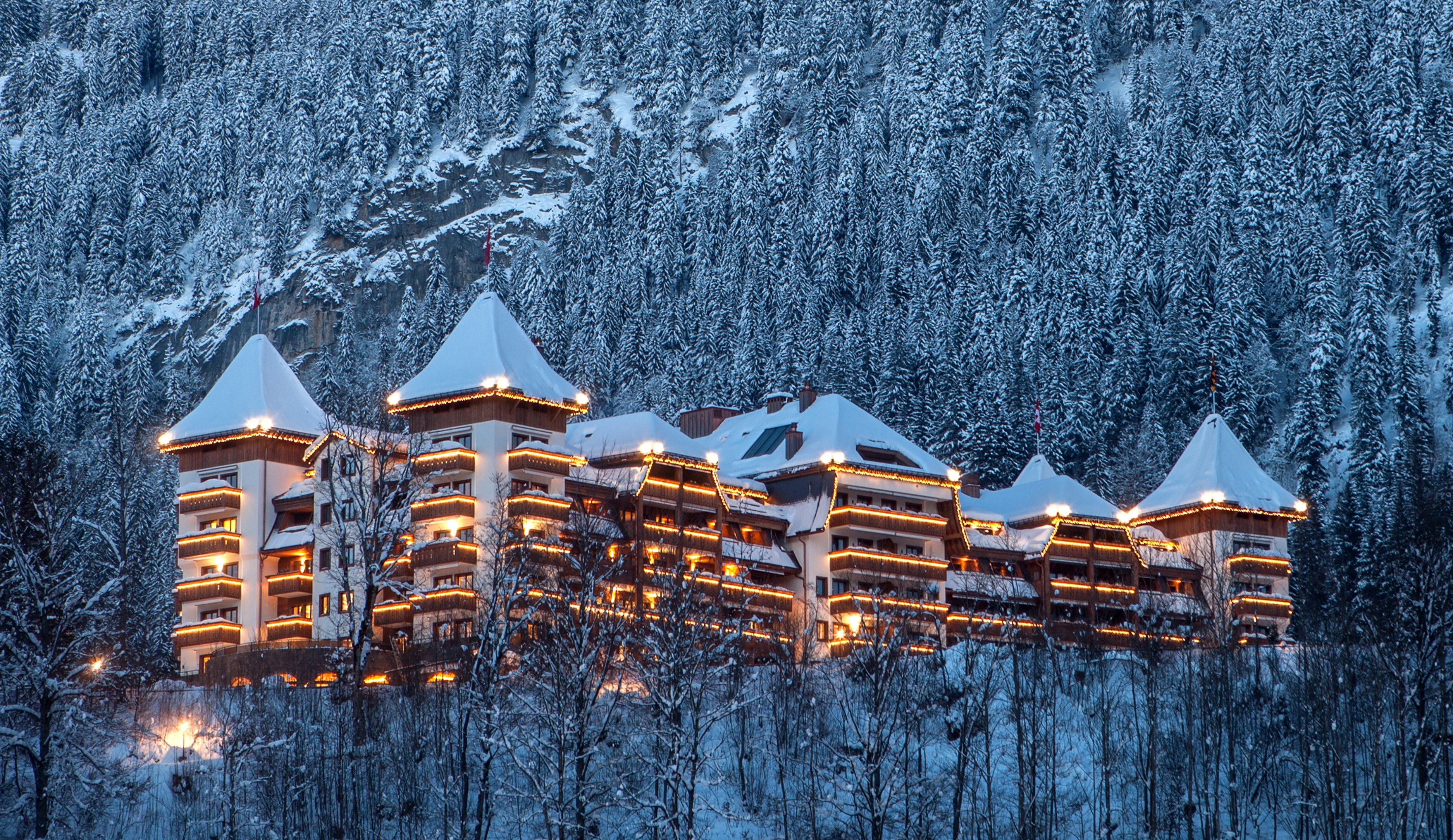 Hotel exterior in winter evening in snowy forest at The Alpina Gstaad, Gstaad, Switzerland