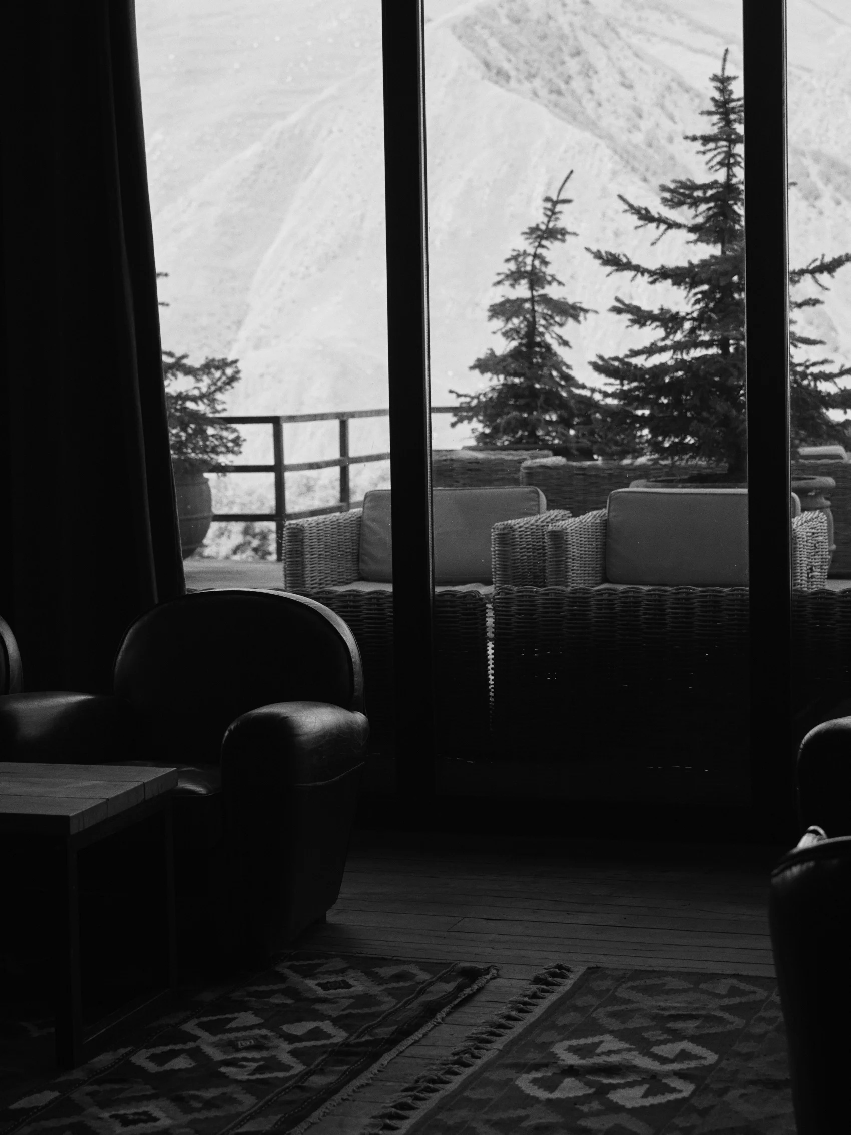Black-and-white lounge interior looking past terrace seating towards snowy mountains at Rooms Hotel Kazbegi, Georgia