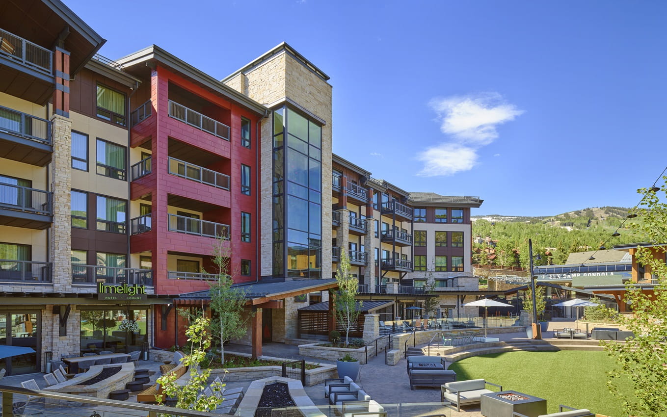 Limelight Hotel Snowmass overlooking Base Village plaza beneath blue skies in Colorado.