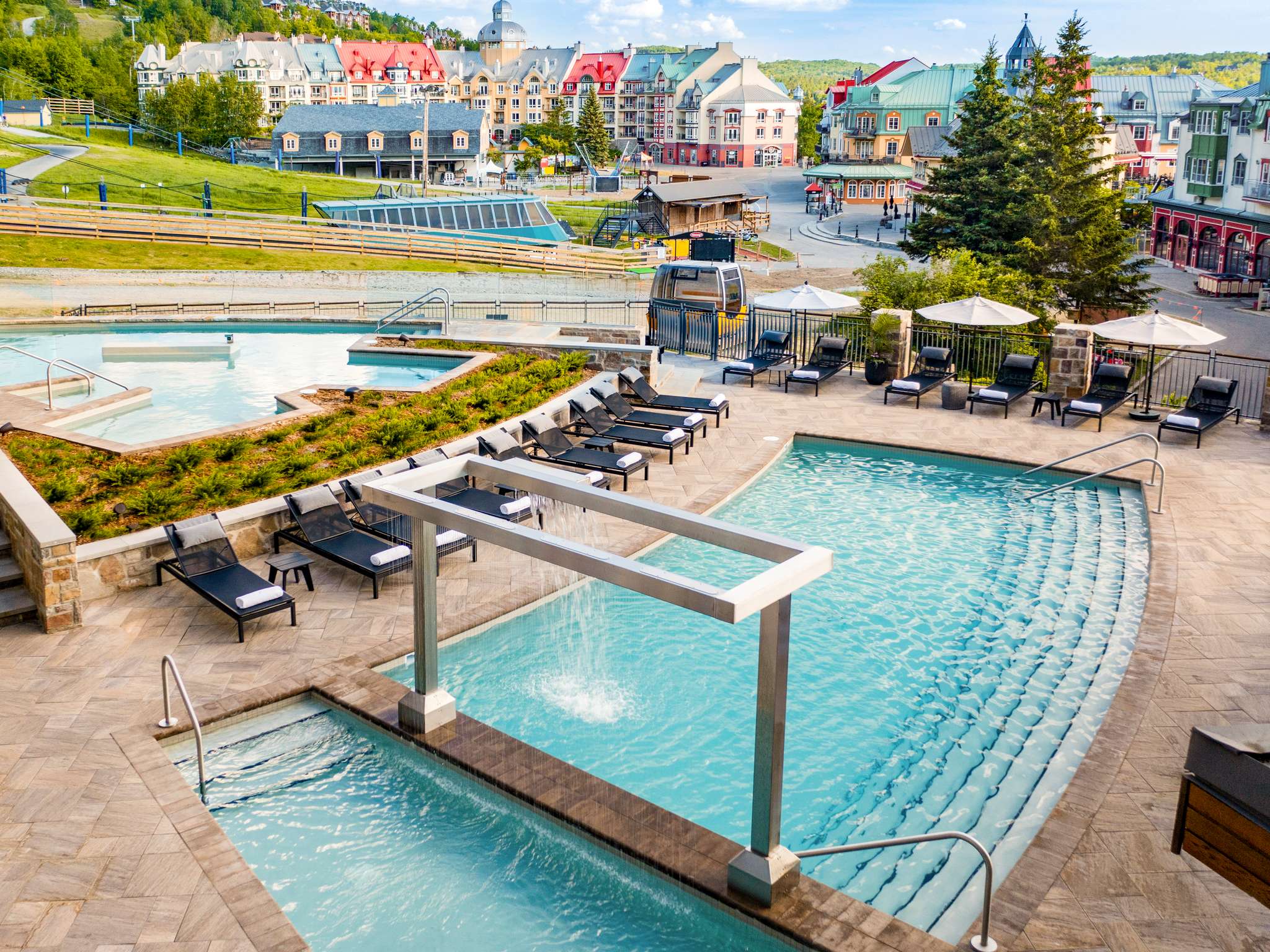 Outdoor swimming pools and poolside loungers at Fairmont Tremblant, overlooking the pedestrian village in summer.