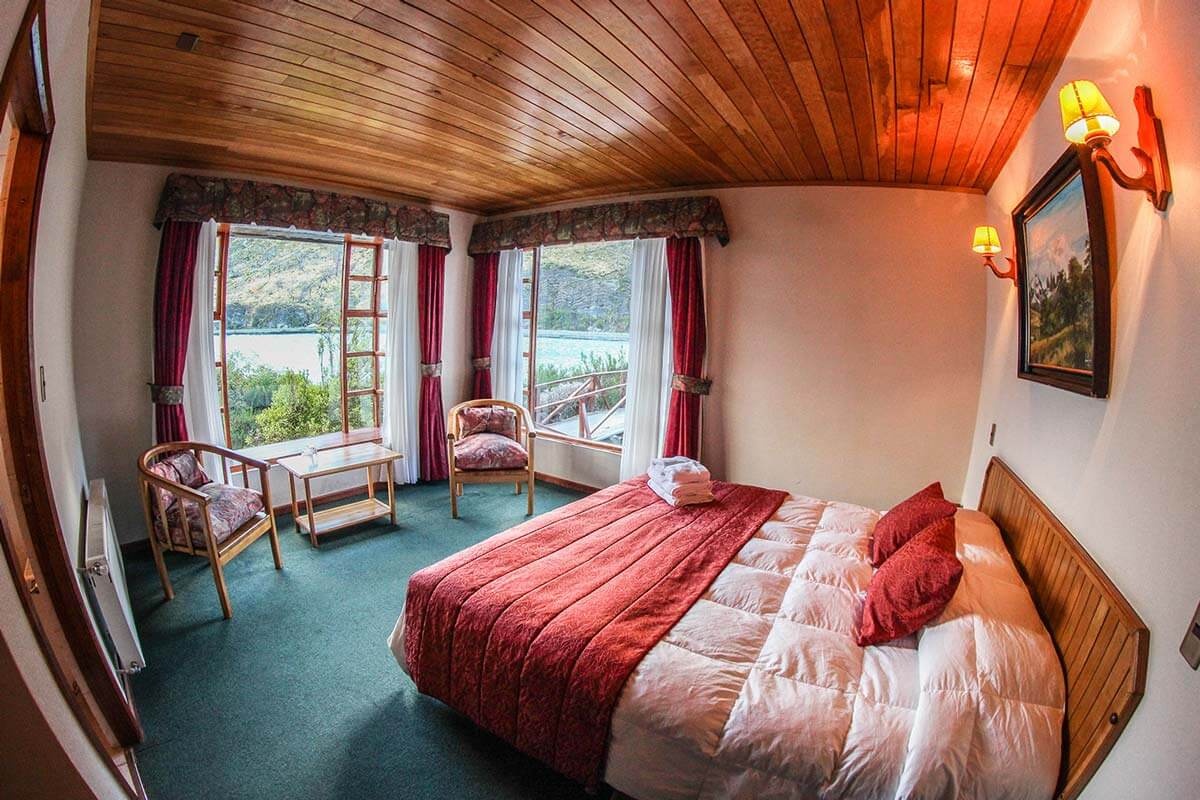 Double bedroom with wood ceiling, red bed runner and lake-facing seating.