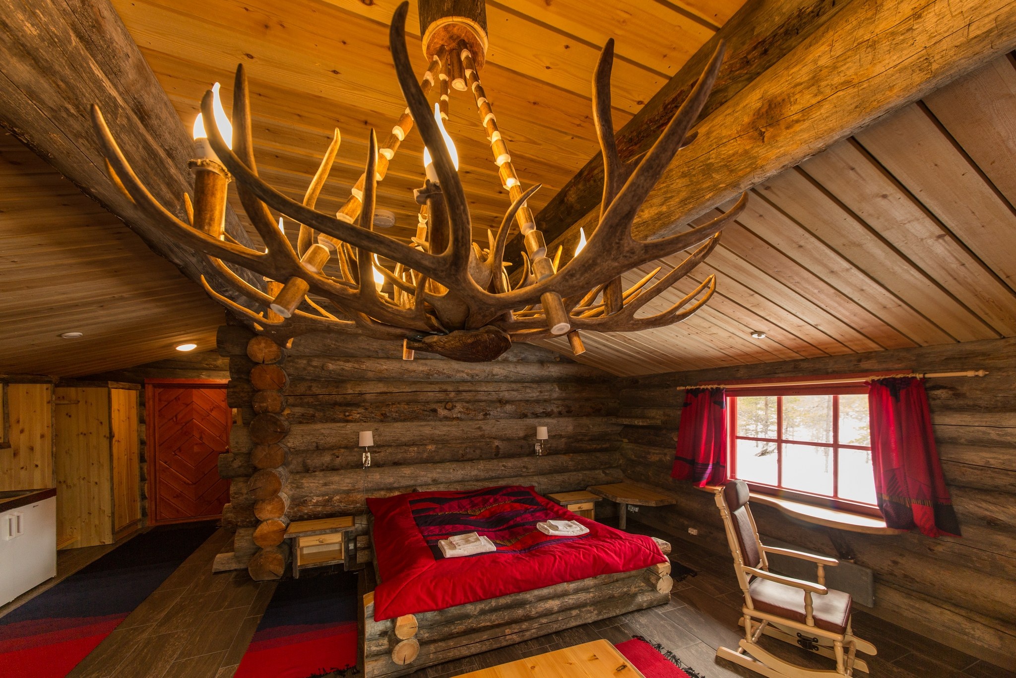 Log cabin bedroom with red bedding and an antler chandelier at Kakslauttanen Arctic Resort, Saariselkä, Finnish Lapland