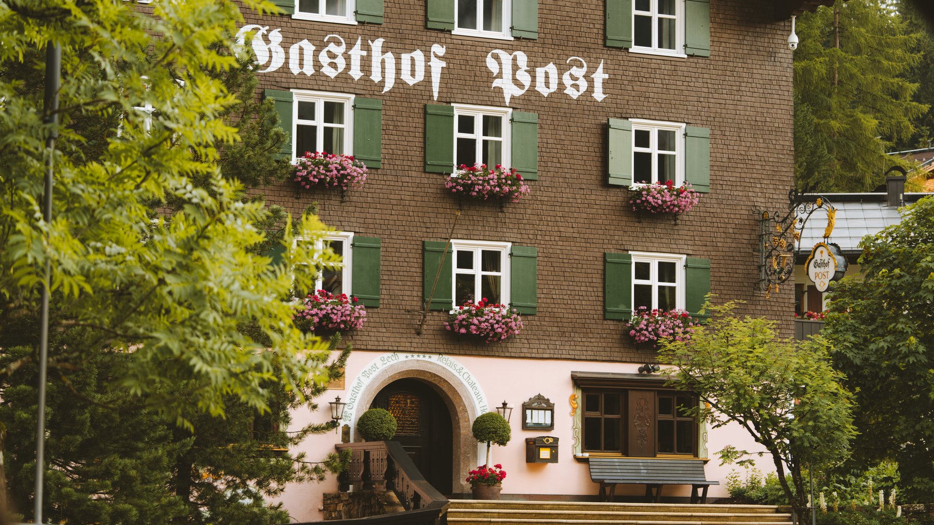 Post Lech Arlberg facade with green shutters and summer flower boxes