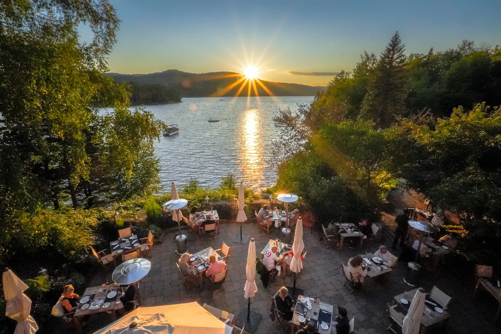Outdoor communal dining terrace with tables and chairs overlooking the lake at sunset at Hôtel Quintessence