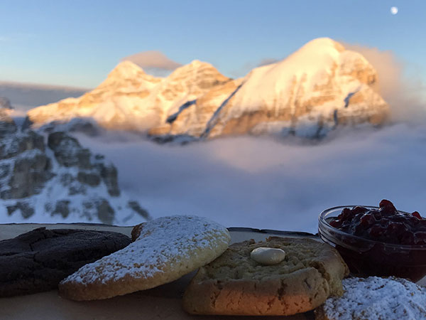 Pastries and a hot drink set against sunlit snow-covered Dolomite peaks at Rifugio Lagazuoi, Dolomites, Italy
