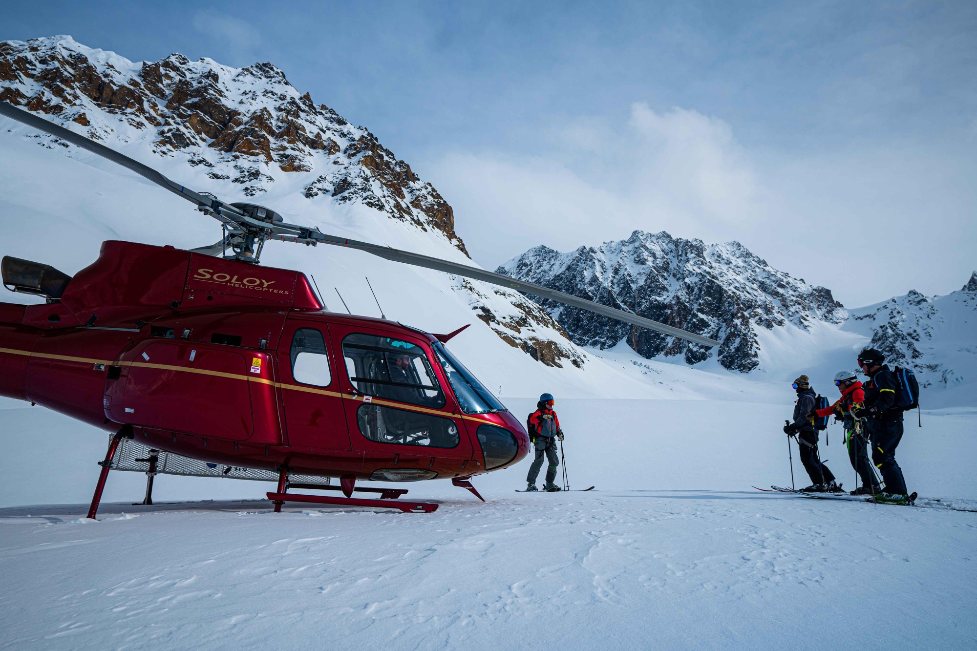 Helicopter and skiers on a snowy mountain ridge, Tordrillo Mountain Lodge, Alaska, USA