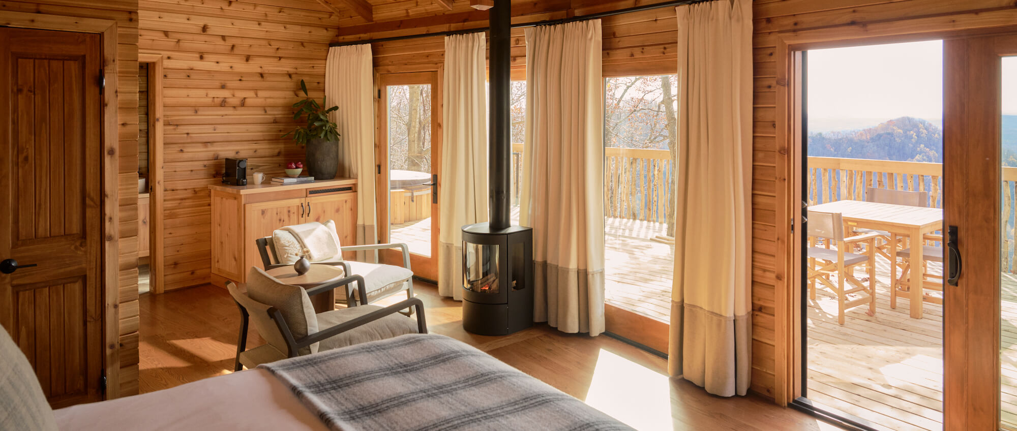 Wood-panelled bedroom with a black stove and glass doors onto a mountain-view deck at Primland, Virginia, USA