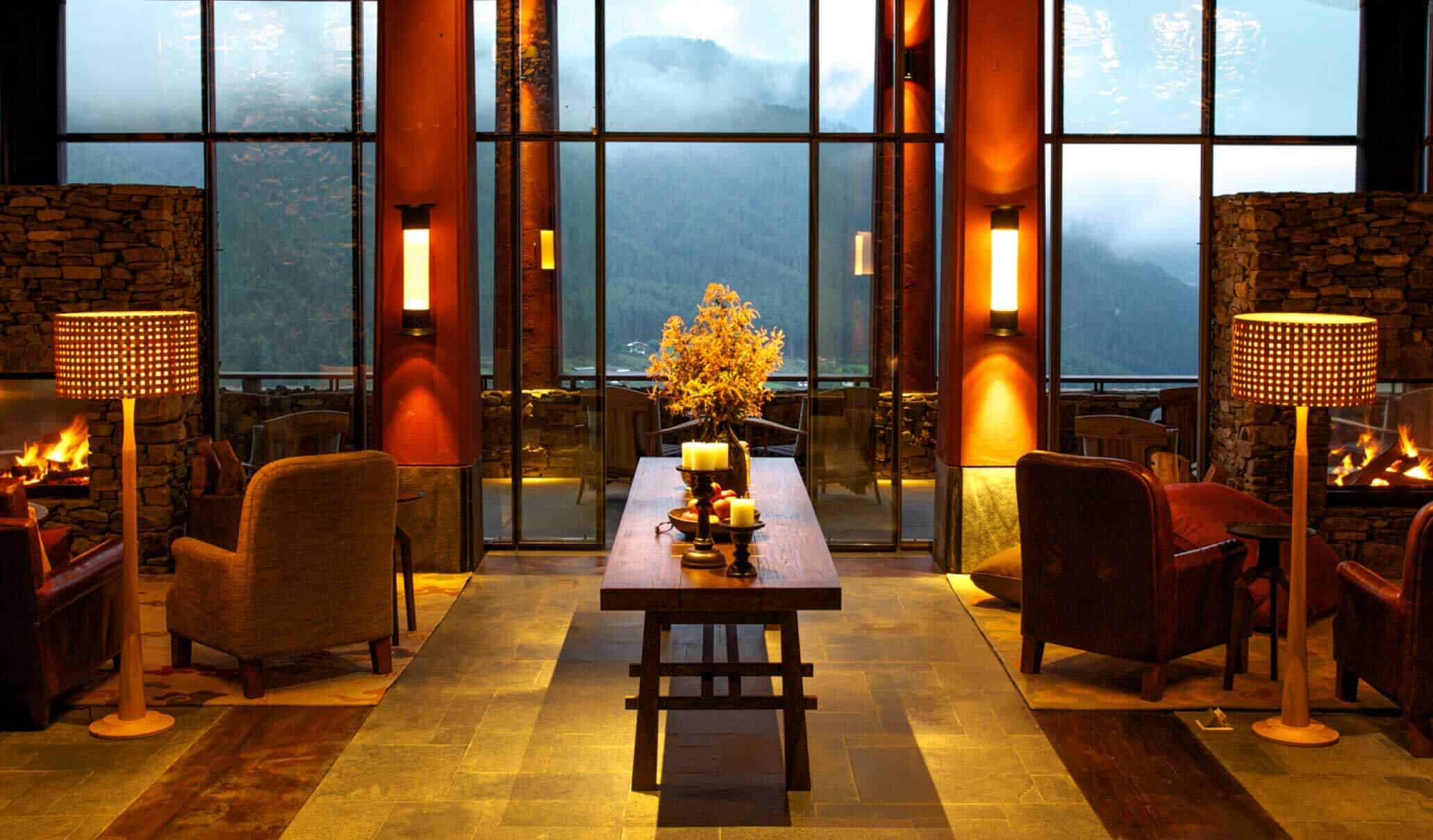 Main lodge lounge at Gangtey Lodge with tall timber beams, stone fireplaces and windows overlooking the valley