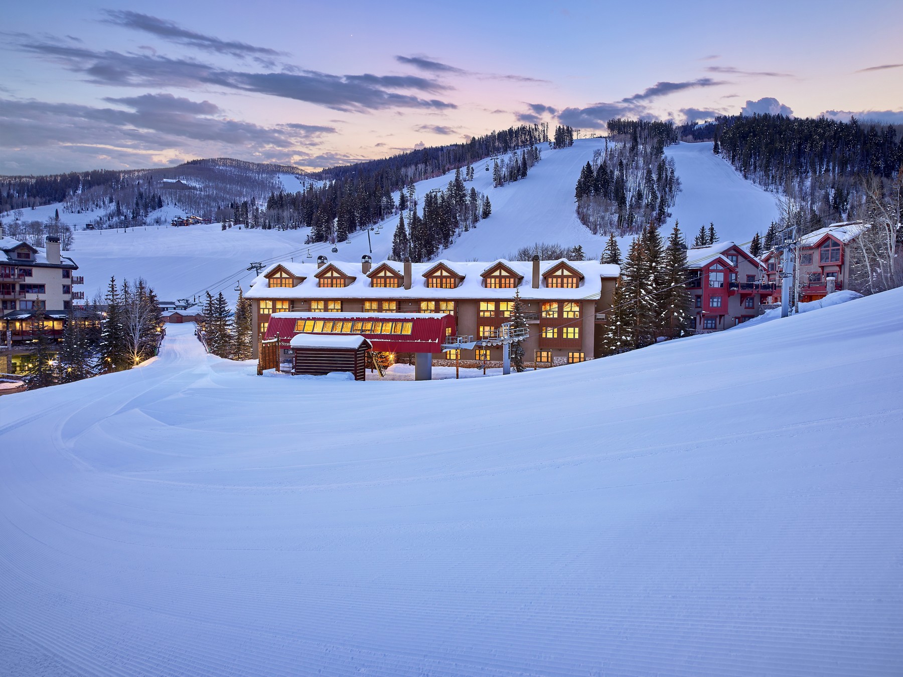 The Osprey at Beaver Creek illuminated beside snow-covered ski slopes at dusk.