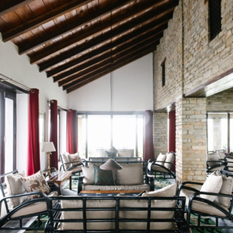 Lounge seating beneath exposed wooden rafters beside stone walls and broad windows at Tiger Mountain Pokhara Lodge, Nepal