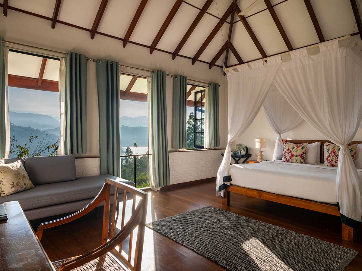 Lake-view suite with a four-poster bed and seating beside the windows at Camellia Hills, Sri Lanka