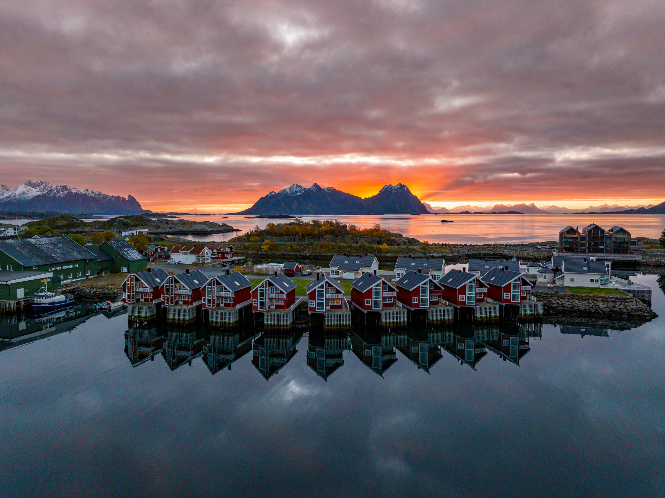 Elevated sunset view of waterfront cabins reflected in calm harbour water at Svinøya Rorbuer, Lofoten, Norway