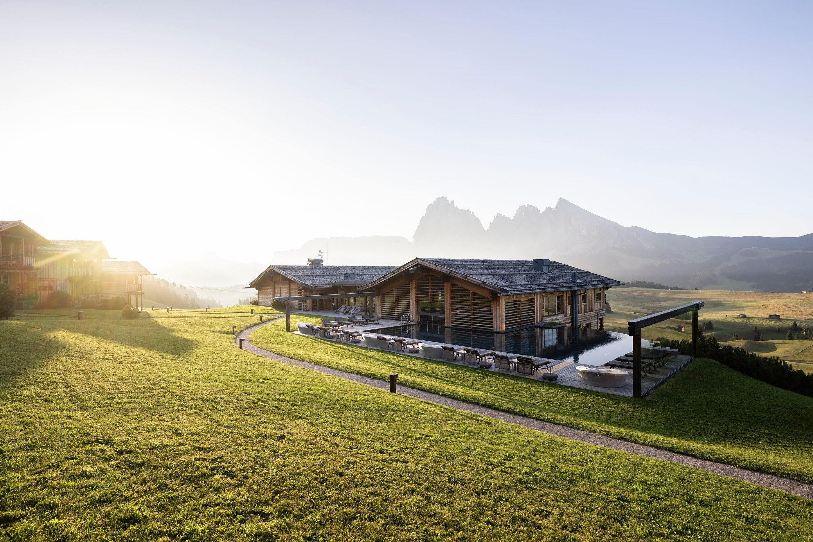 Timber lodge buildings on alpine meadows with Dolomite peaks beyond at Adler Mountain Lodge, Alpe di Siusi (Seiser Alm)