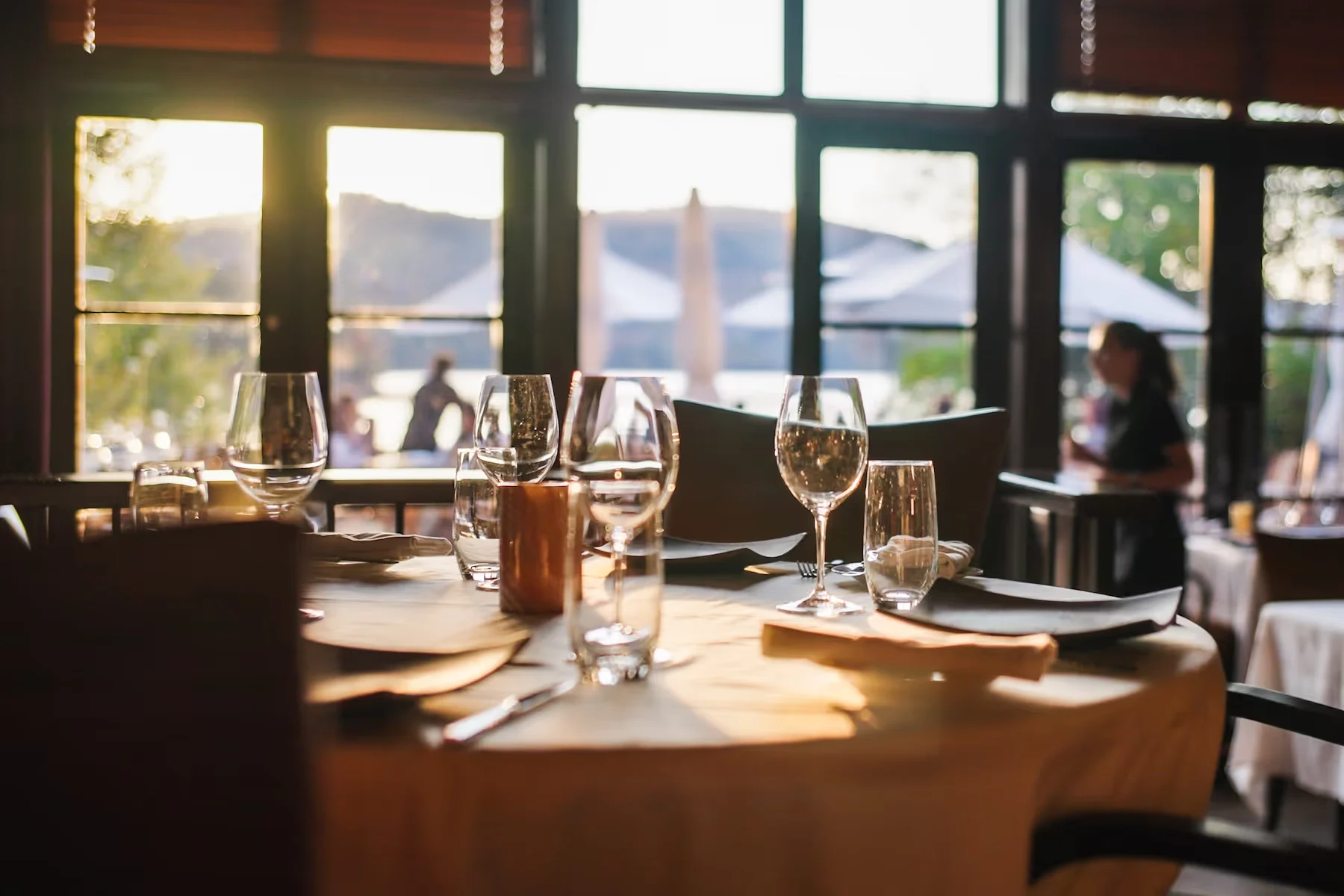Restaurant table set with wine glasses beside large windows overlooking the lake at Hôtel Quintessence