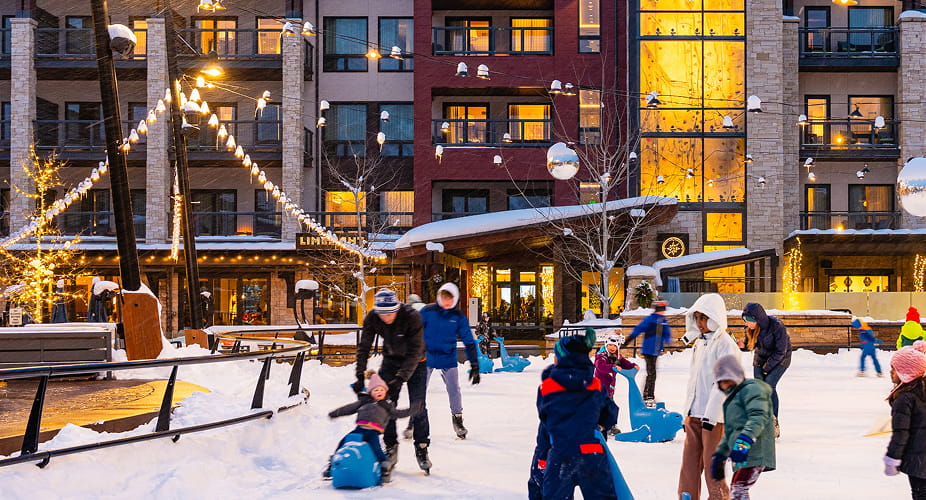 Families skating on the illuminated Base Village ice rink outside Limelight Hotel Snowmass.