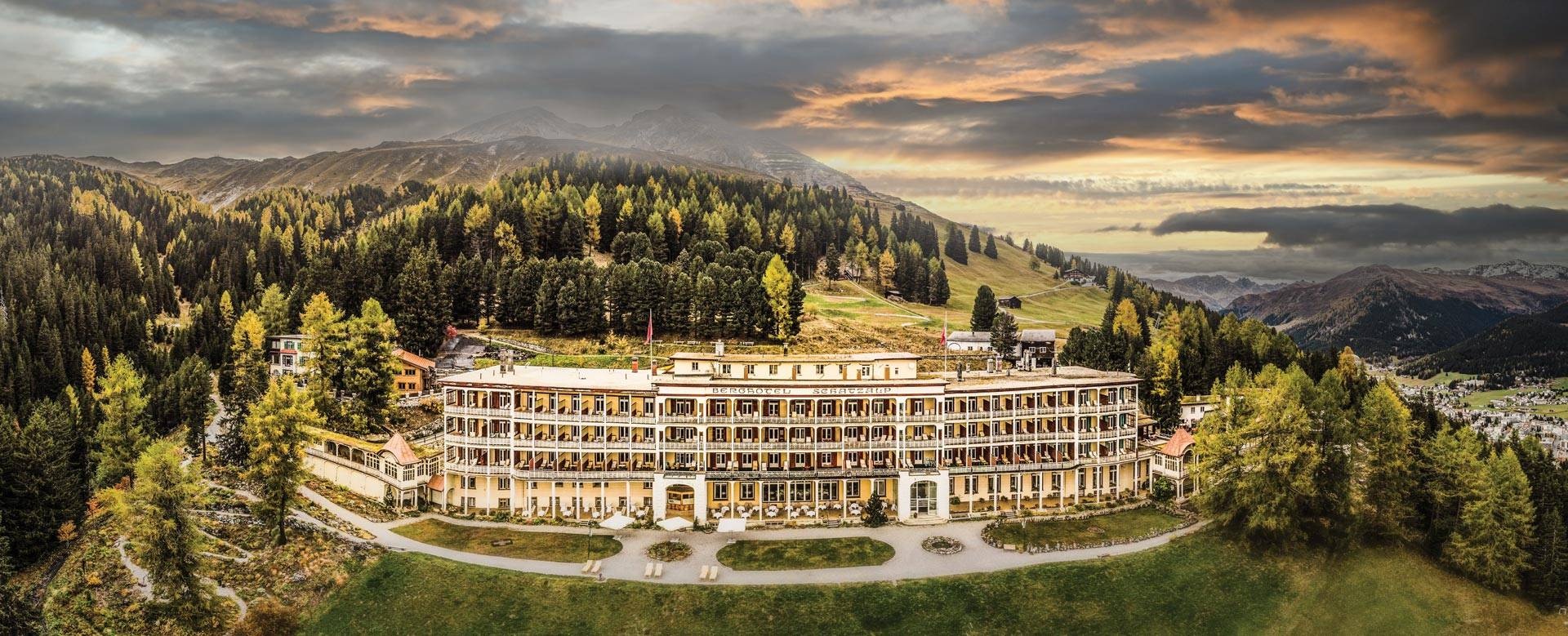 Long white Schatzalp hotel surrounded by forest above Davos at sunset.