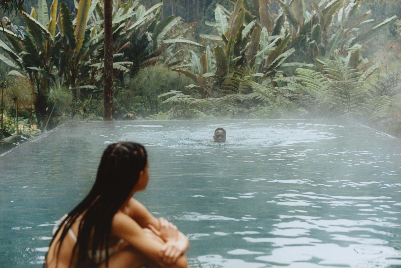 Guests relaxing in a steaming outdoor pool surrounded by tropical foliage, One&Only Gorilla's Nest, Volcanoes National Park, Rwanda