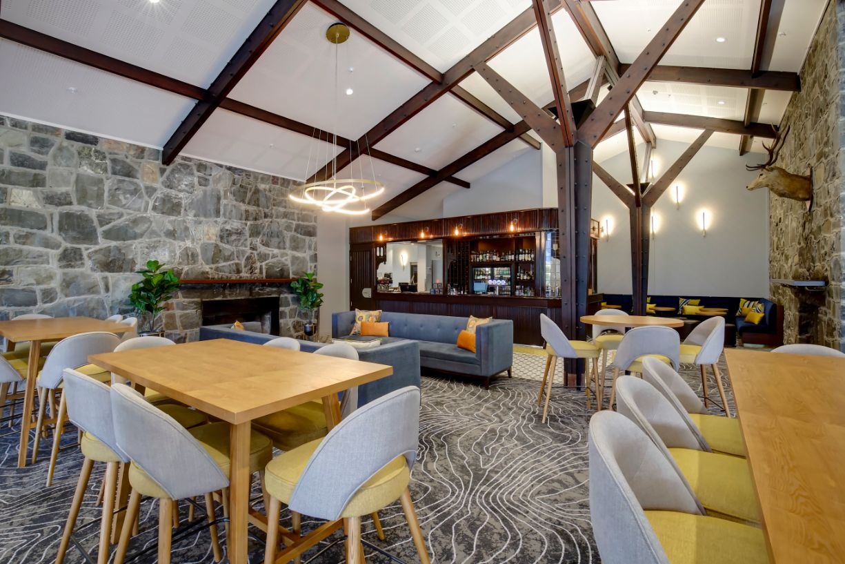 Snowline Bar seating beneath timber beams beside a stone wall and fireplace at The Hermitage Hotel, Aoraki/Mount Cook