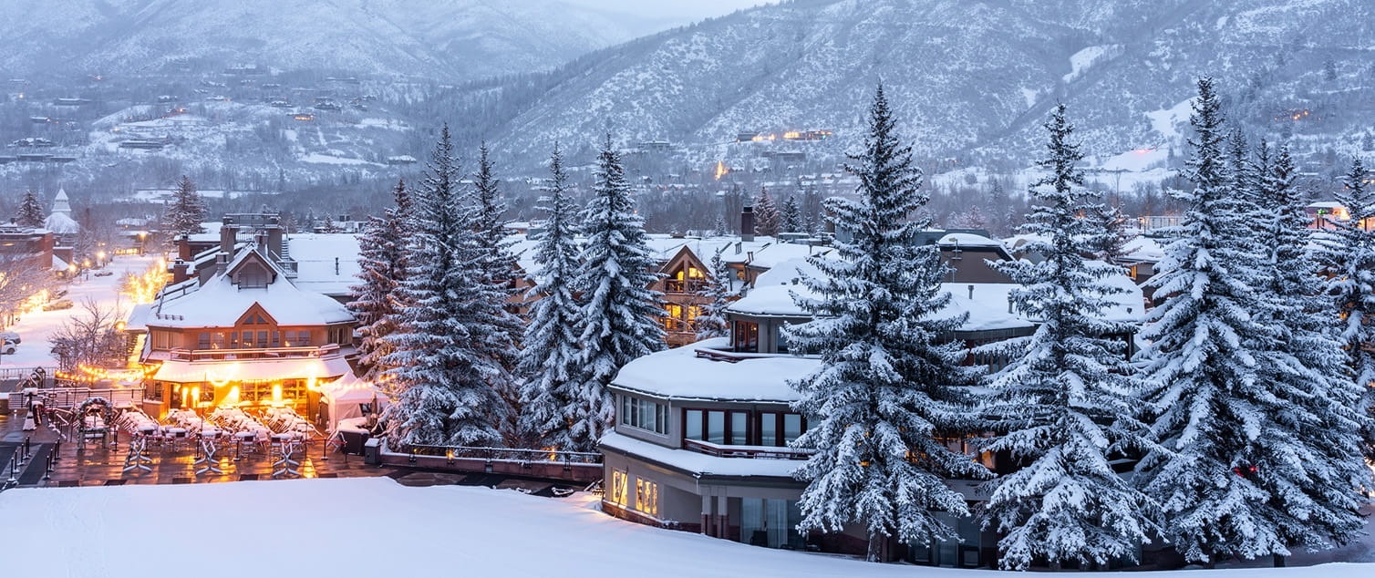 Snowy hotel buildings and trees below Aspen mountain slopes at The Little Nell, Aspen, USA